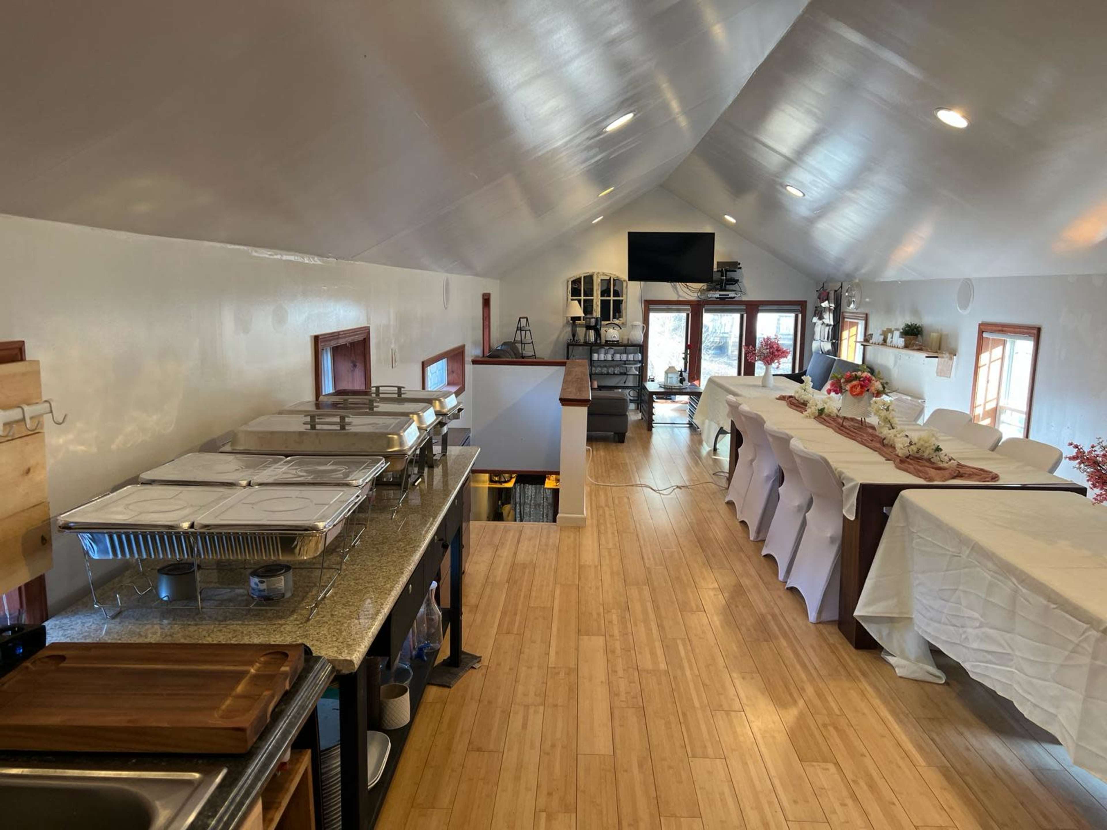 A spacious indoor venue with neatly arranged tables, catering trays on a counter, and a television screen mounted on the wall.