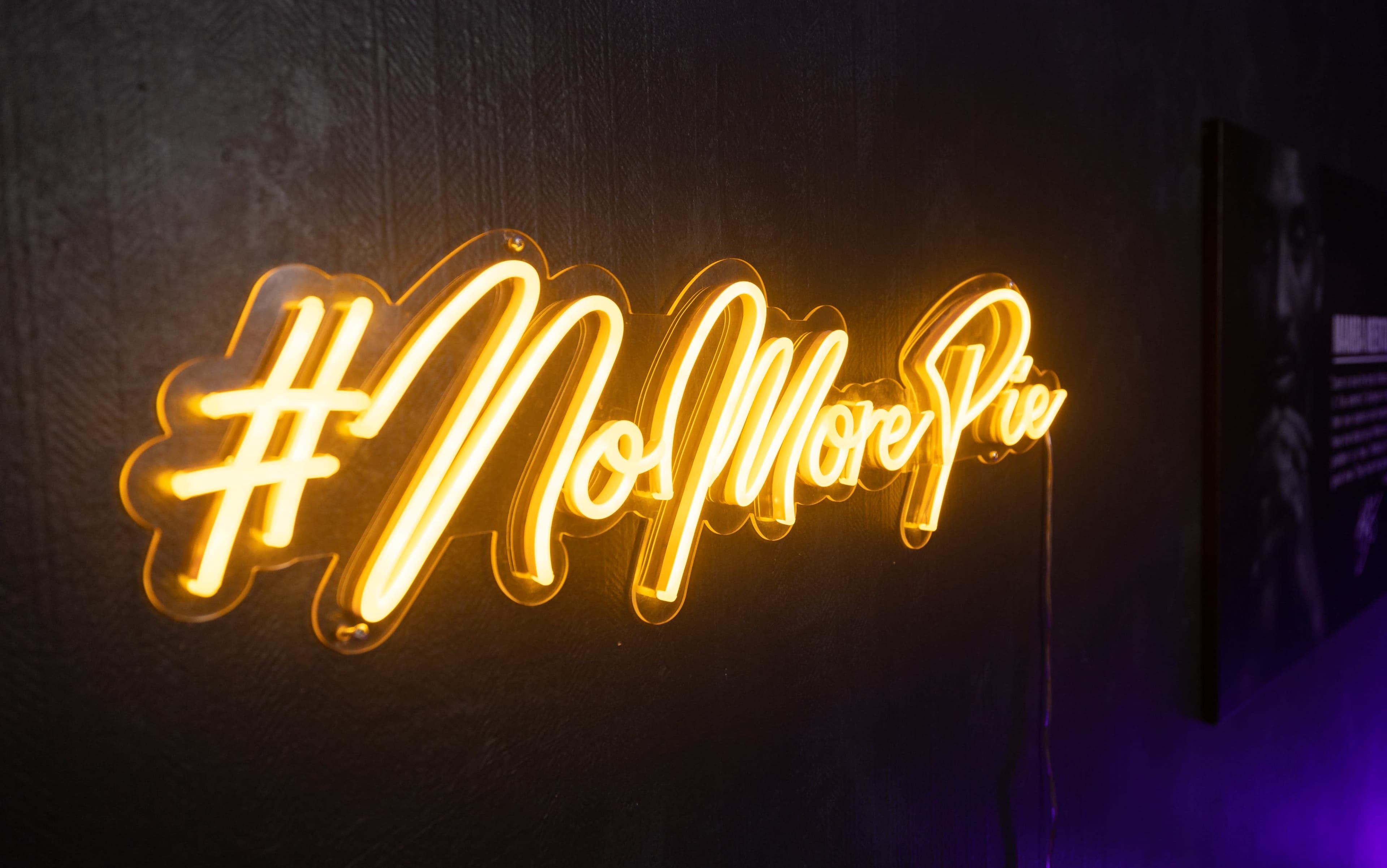 A neon sign displays the text "#NoMorePies" against a dark wall.