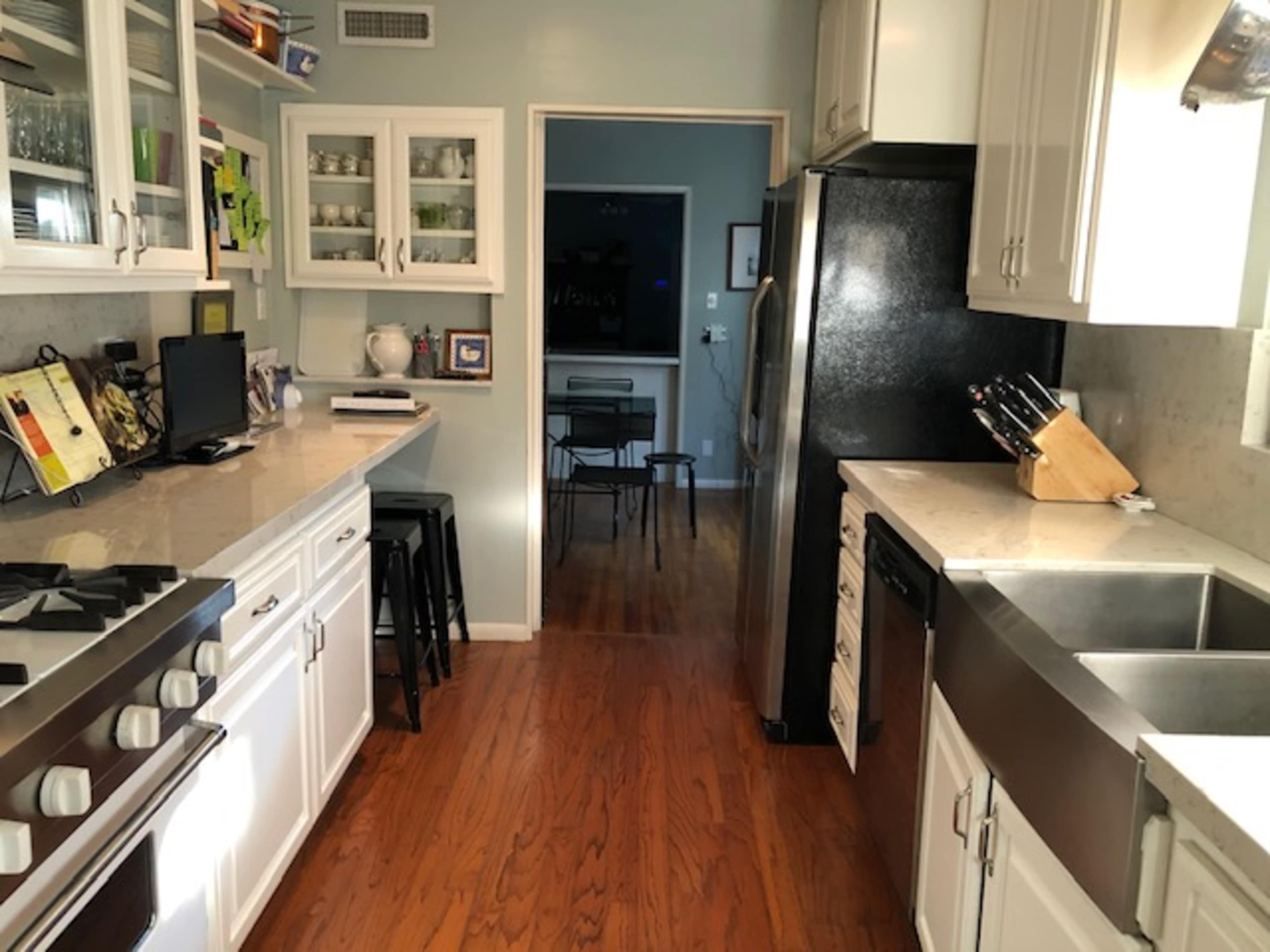 A bright kitchen features white cabinets, a black refrigerator, a stainless steel sink, and a dining area visible in the background.