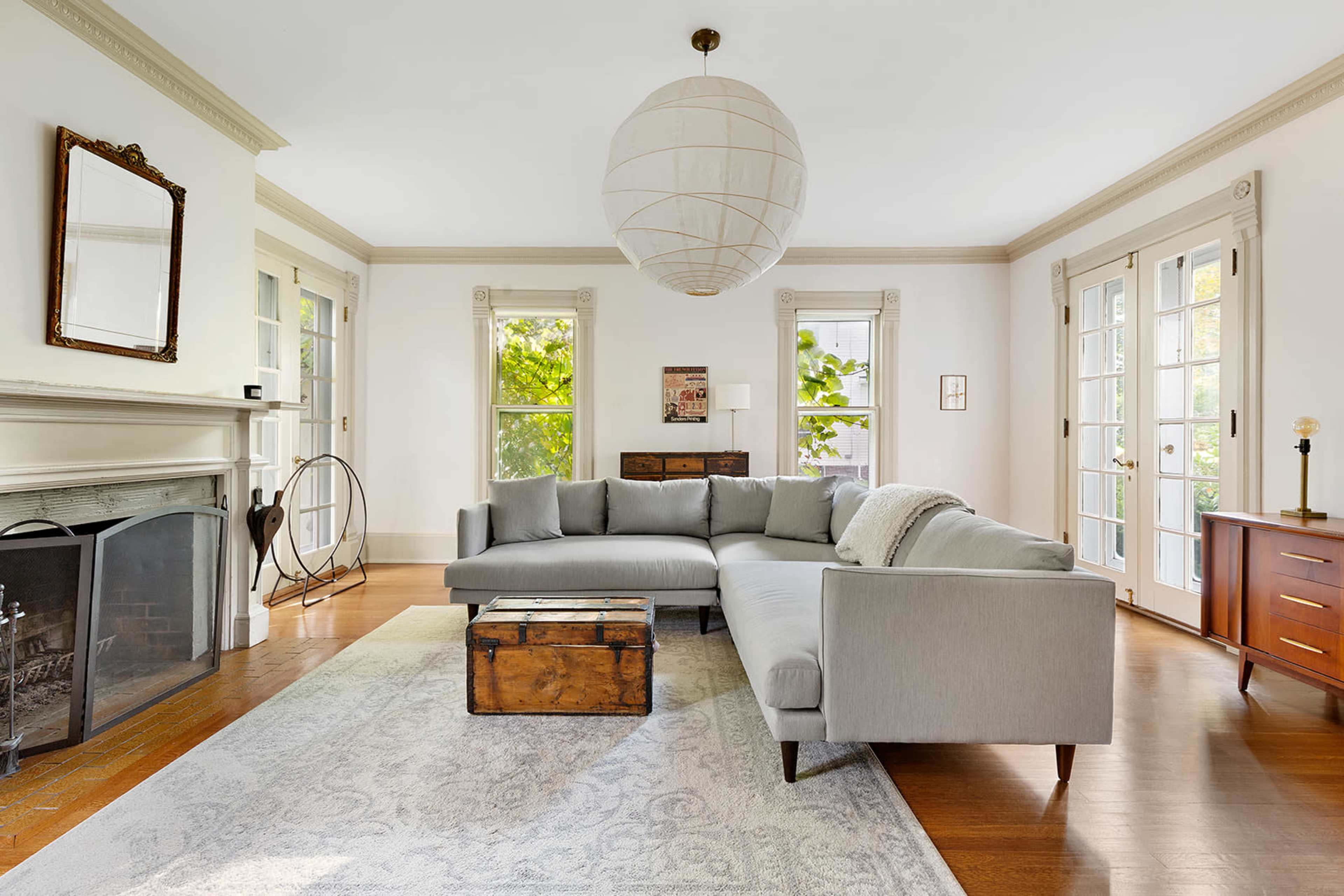 The living room features a gray sectional sofa, a wooden coffee table, a stone fireplace, and large windows that allow natural light in.