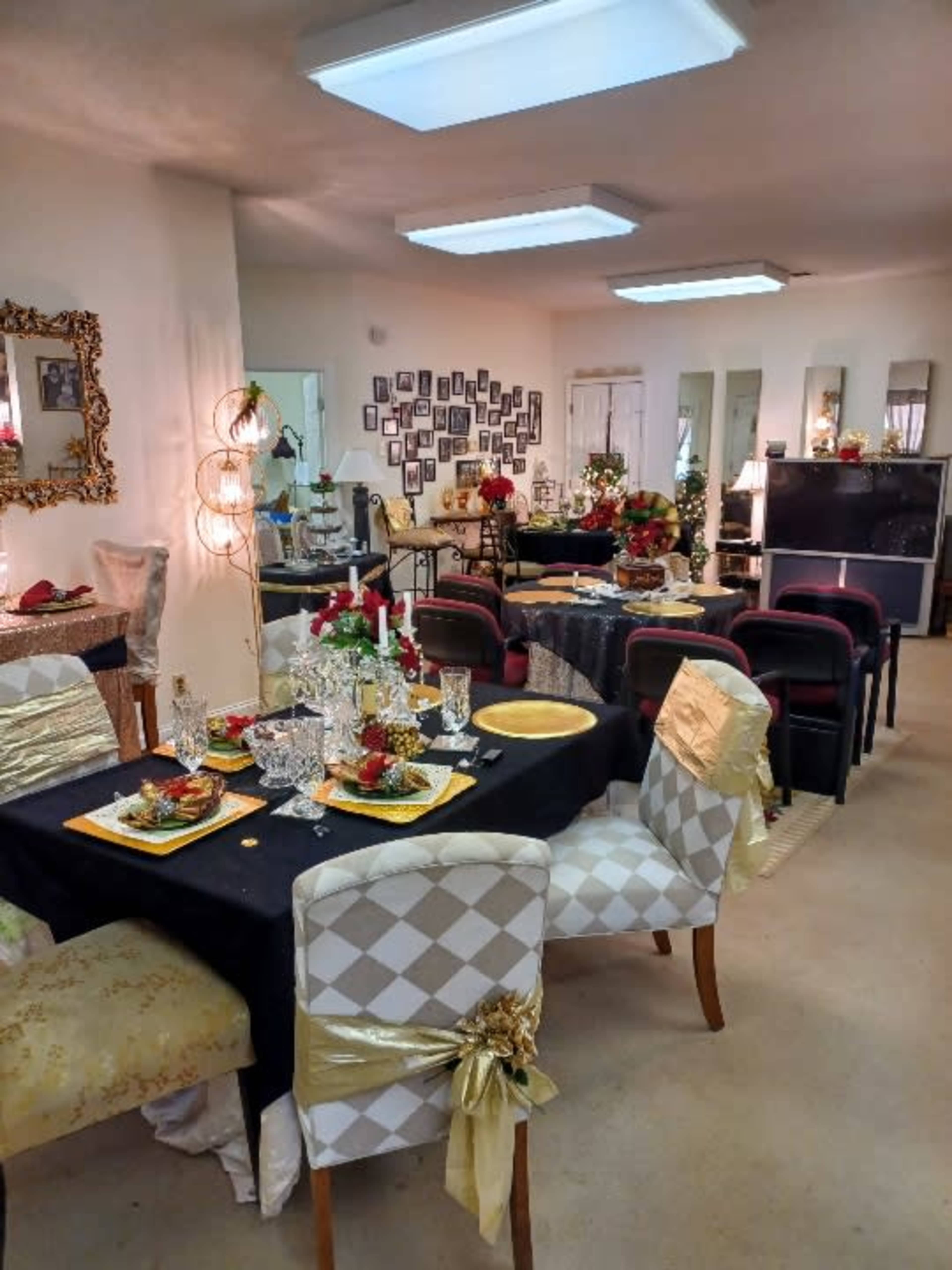 A dining area is set up with multiple tables adorned with floral centerpieces, elegant tableware, and decorative chairs, creating an inviting atmosphere for a gathering.