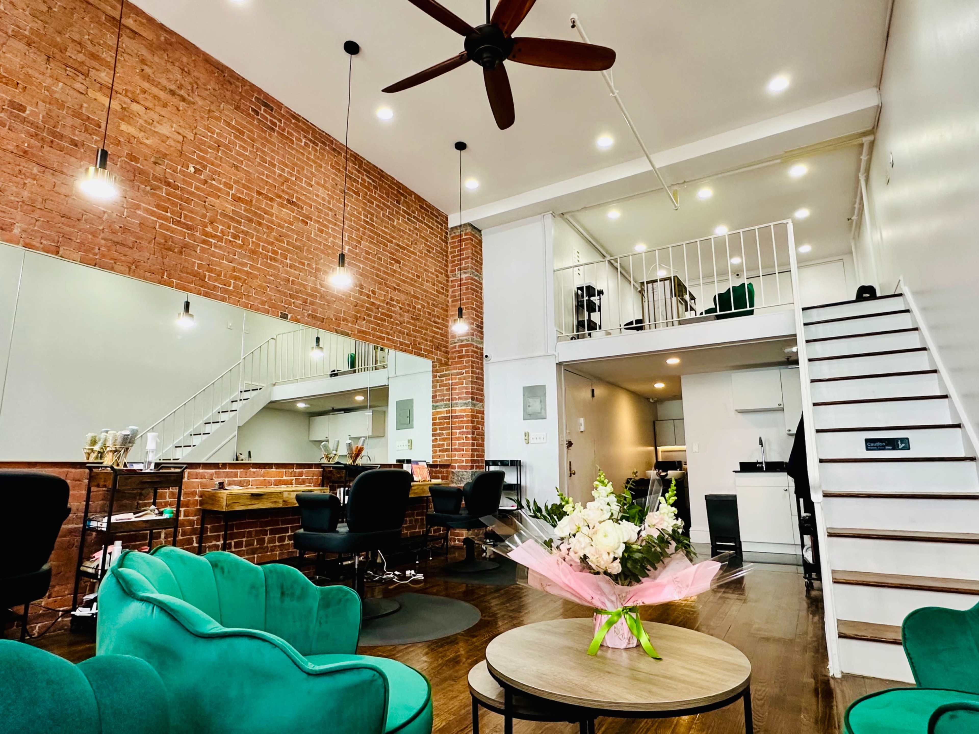 The image shows a stylish interior featuring a brick wall, green seating, a staircase leading to an upper level, and contemporary decor.