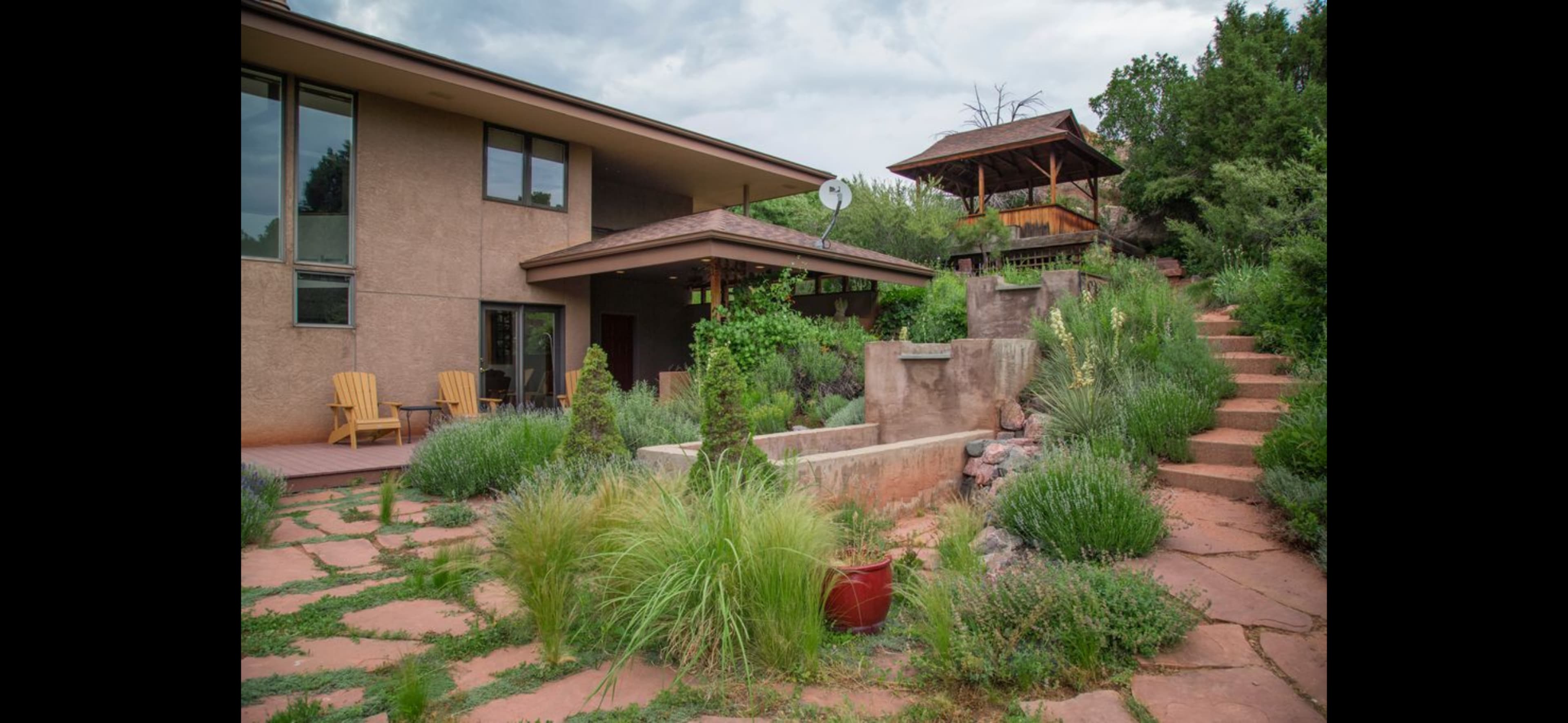 A modern home with a landscaped garden features a stone pathway, planters, and a seating area with chairs.