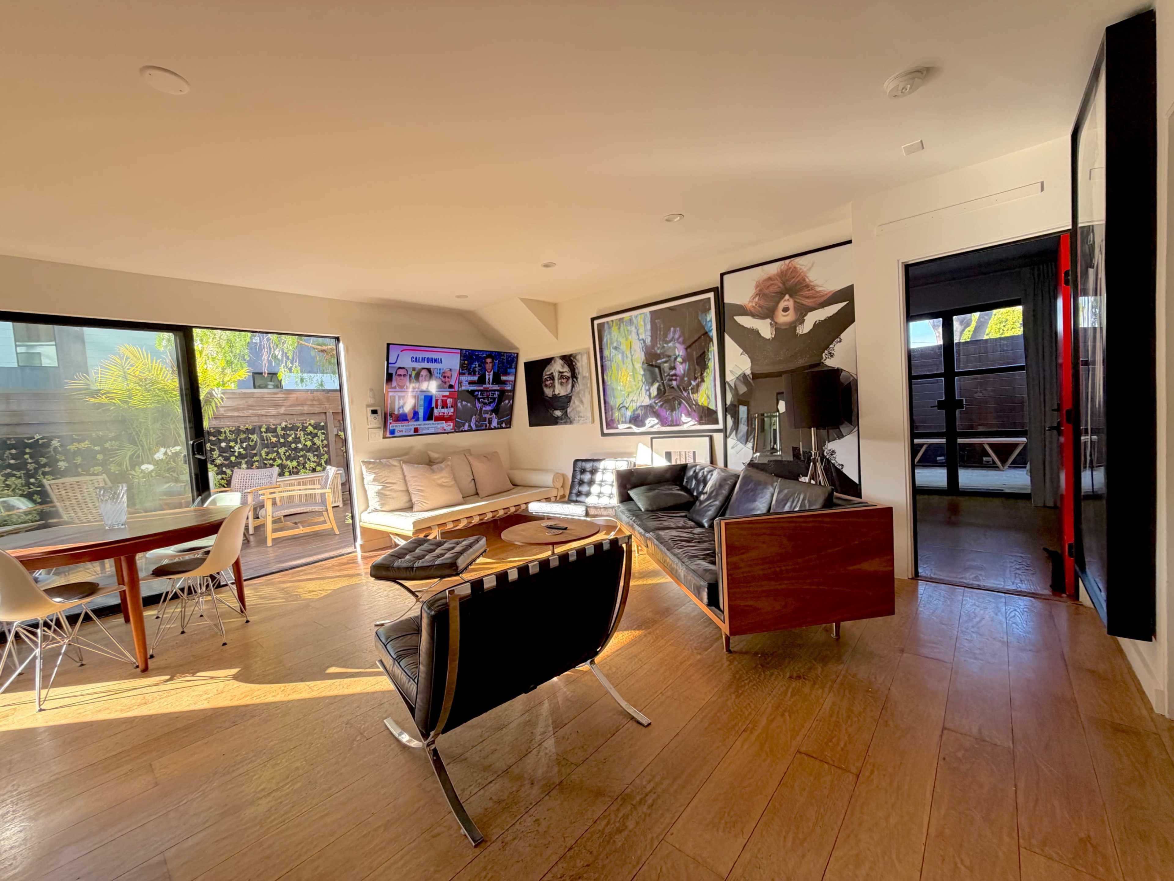 The image shows a modern living room with large windows, comfortable seating, and colorful artwork on the walls.