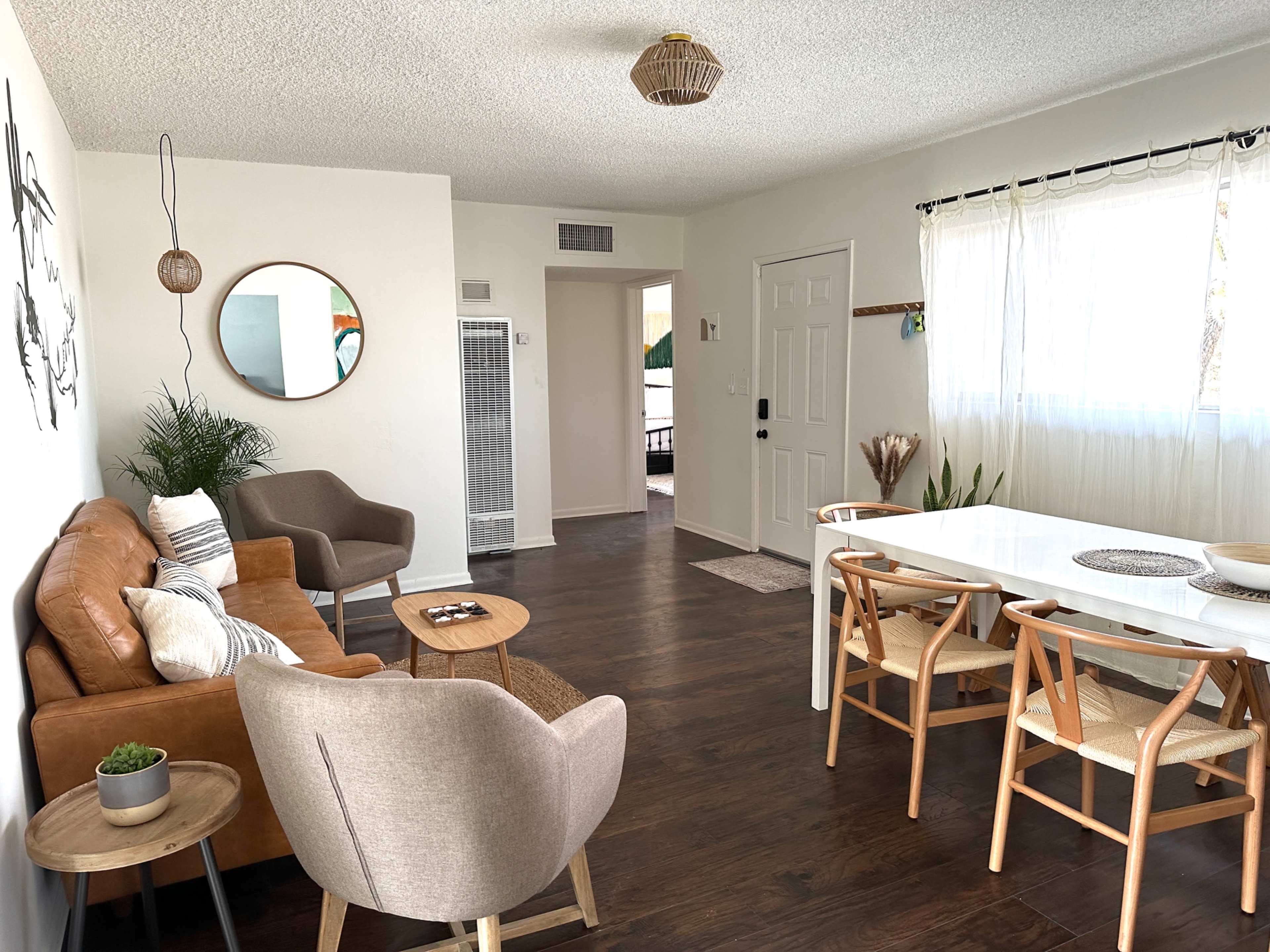 A modern living room and dining area featuring a brown leather sofa, beige armchairs, a white dining table, and a doorway leading to another space.