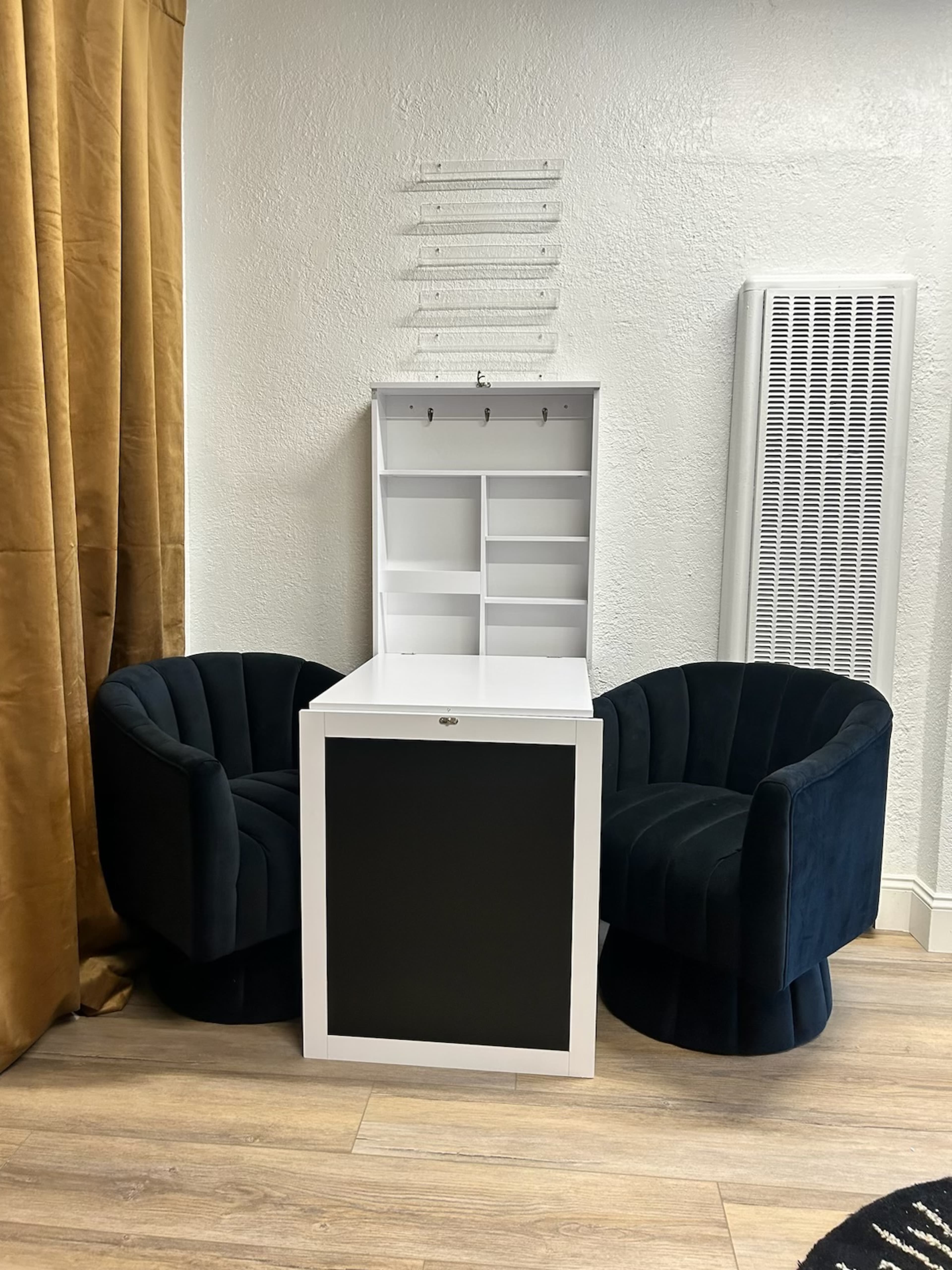 The image shows two blue velvet chairs positioned on either side of a white storage unit with shelves and hooks at the top.