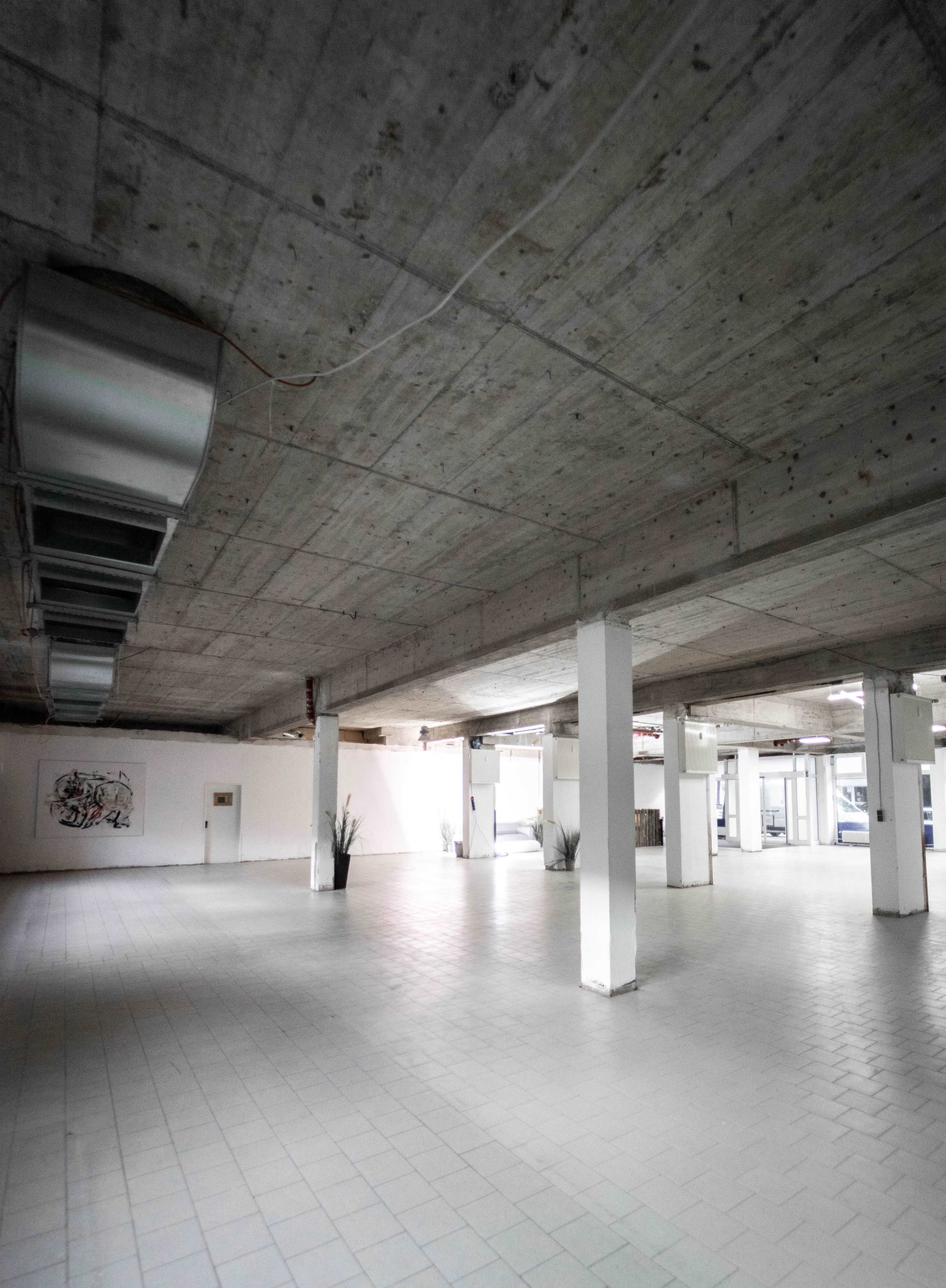 The image shows an empty concrete-floored commercial space with exposed ceilings and minimal decor.