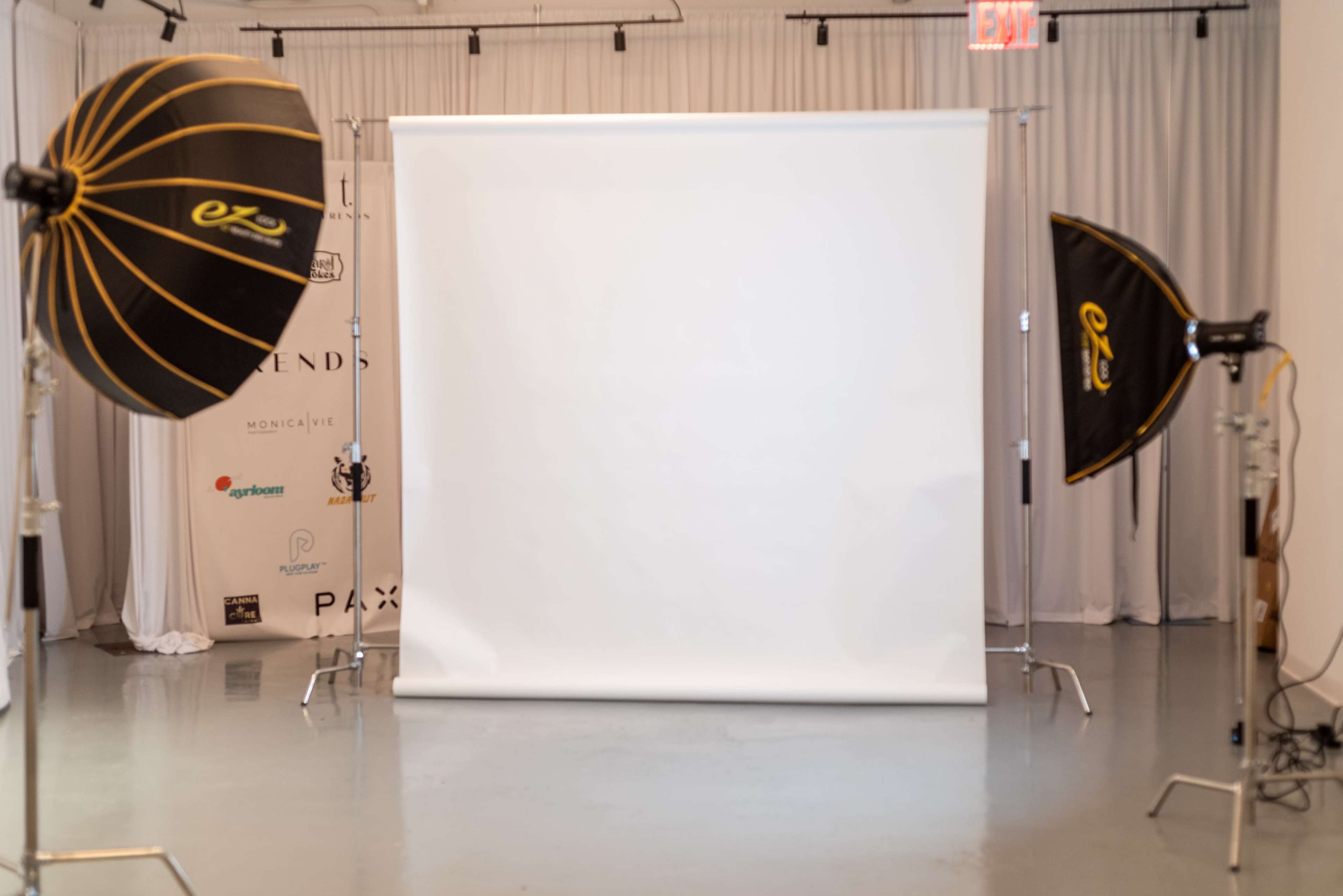The image shows a photography studio setup featuring a blank white backdrop flanked by two large softbox lights on stands.