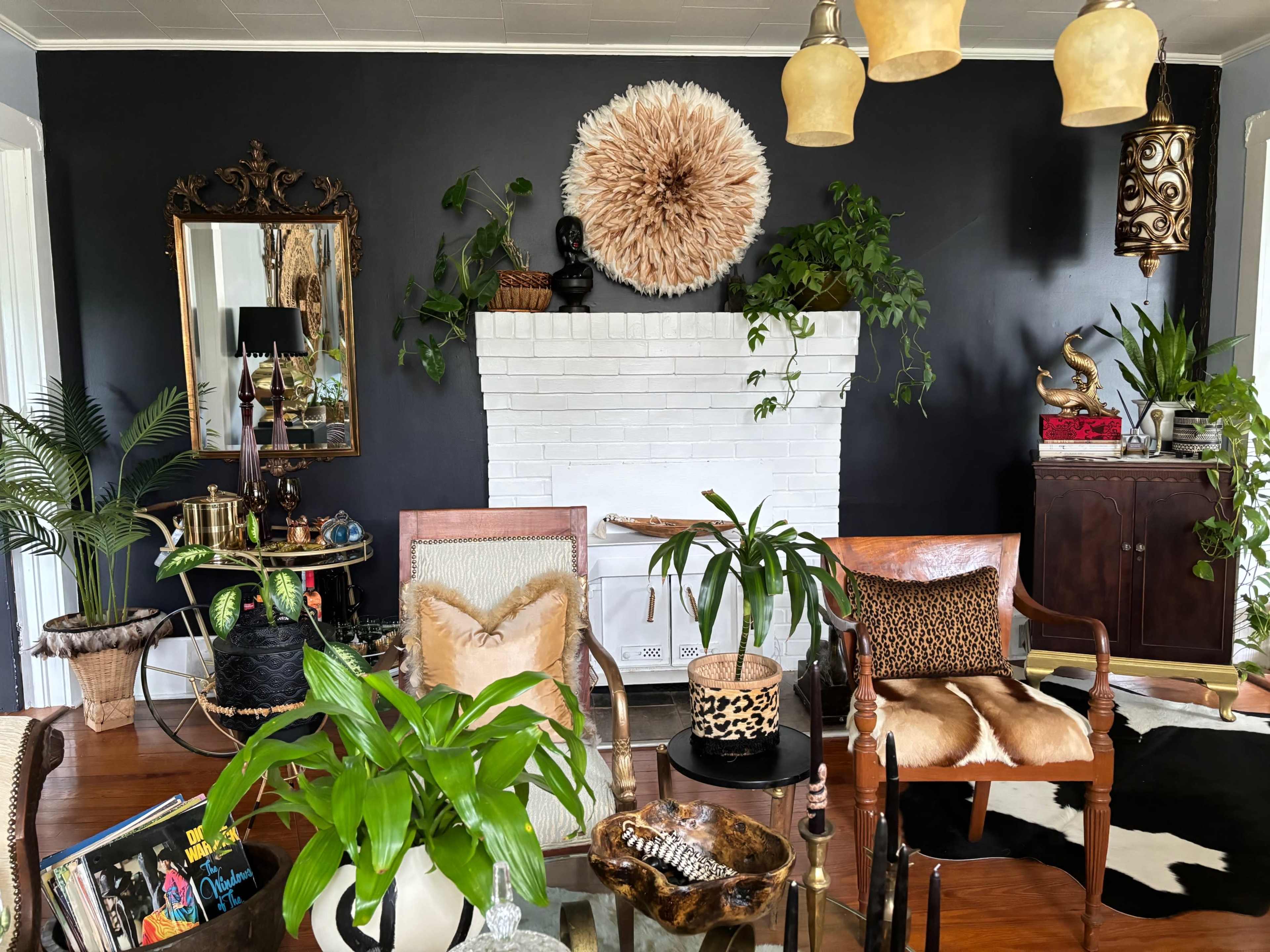 A living room features a white-brick fireplace adorned with a large decorative circular piece, surrounded by various plants and eclectic furniture.
