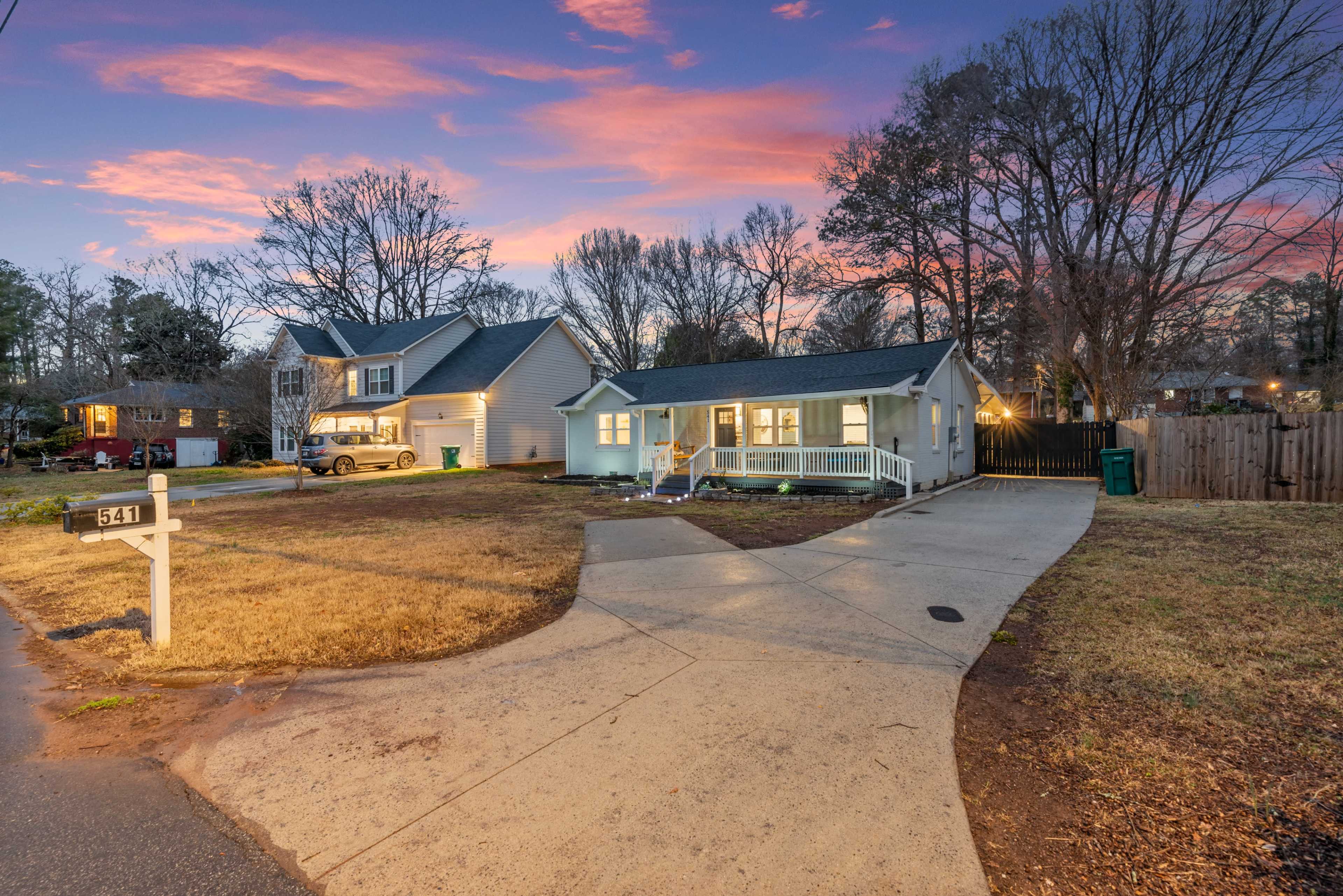 The image shows a residential area at dusk with two houses, a driveway leading to one house, and a mailbox near the street.