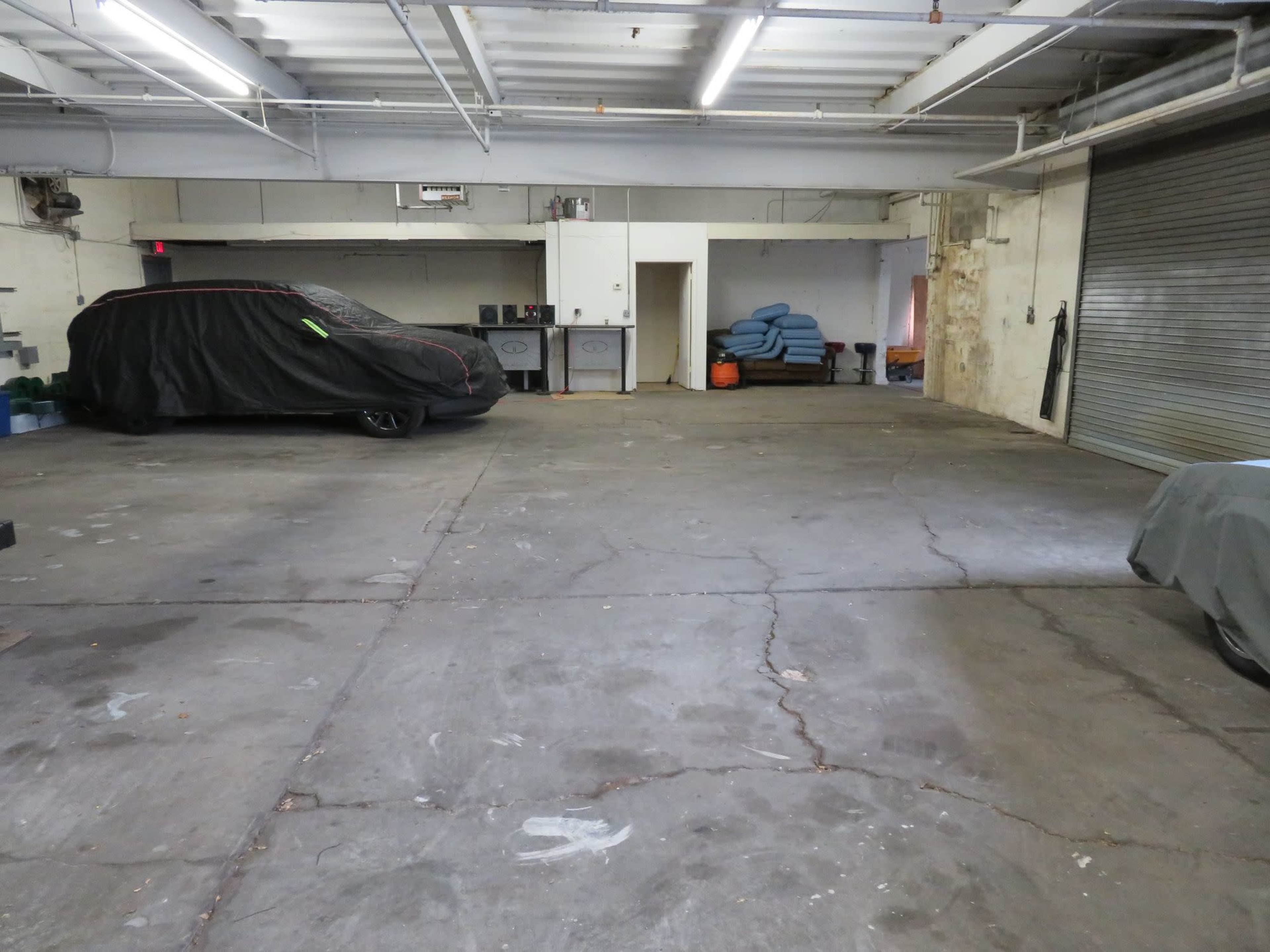 The image shows a spacious garage with two covered cars, a table in the background, and a concrete floor.