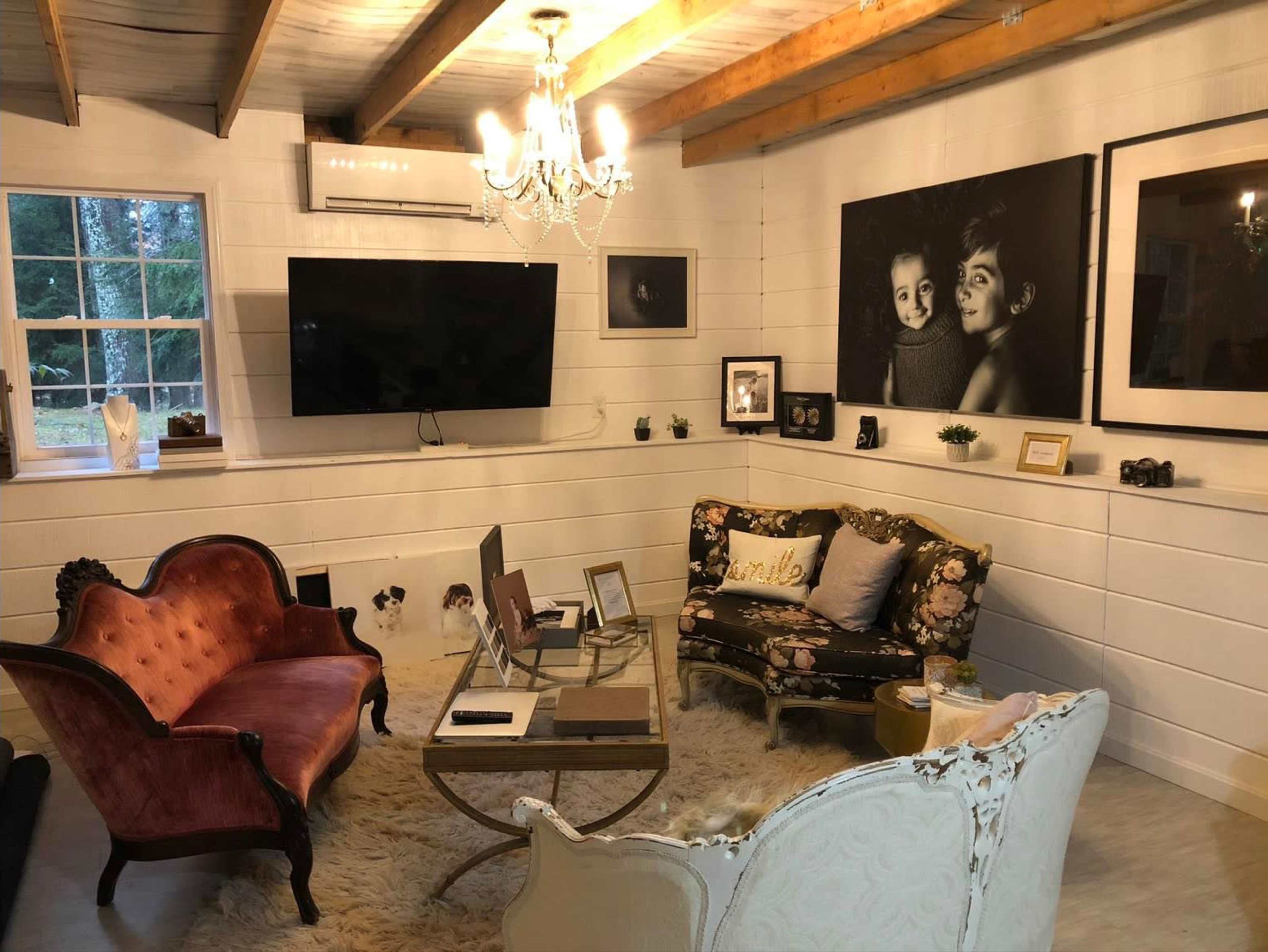 A cozy living area featuring a blend of vintage and modern furniture, including a pink velvet sofa and a floral-patterned couch, with a large TV and framed photos on the white shiplap wall.