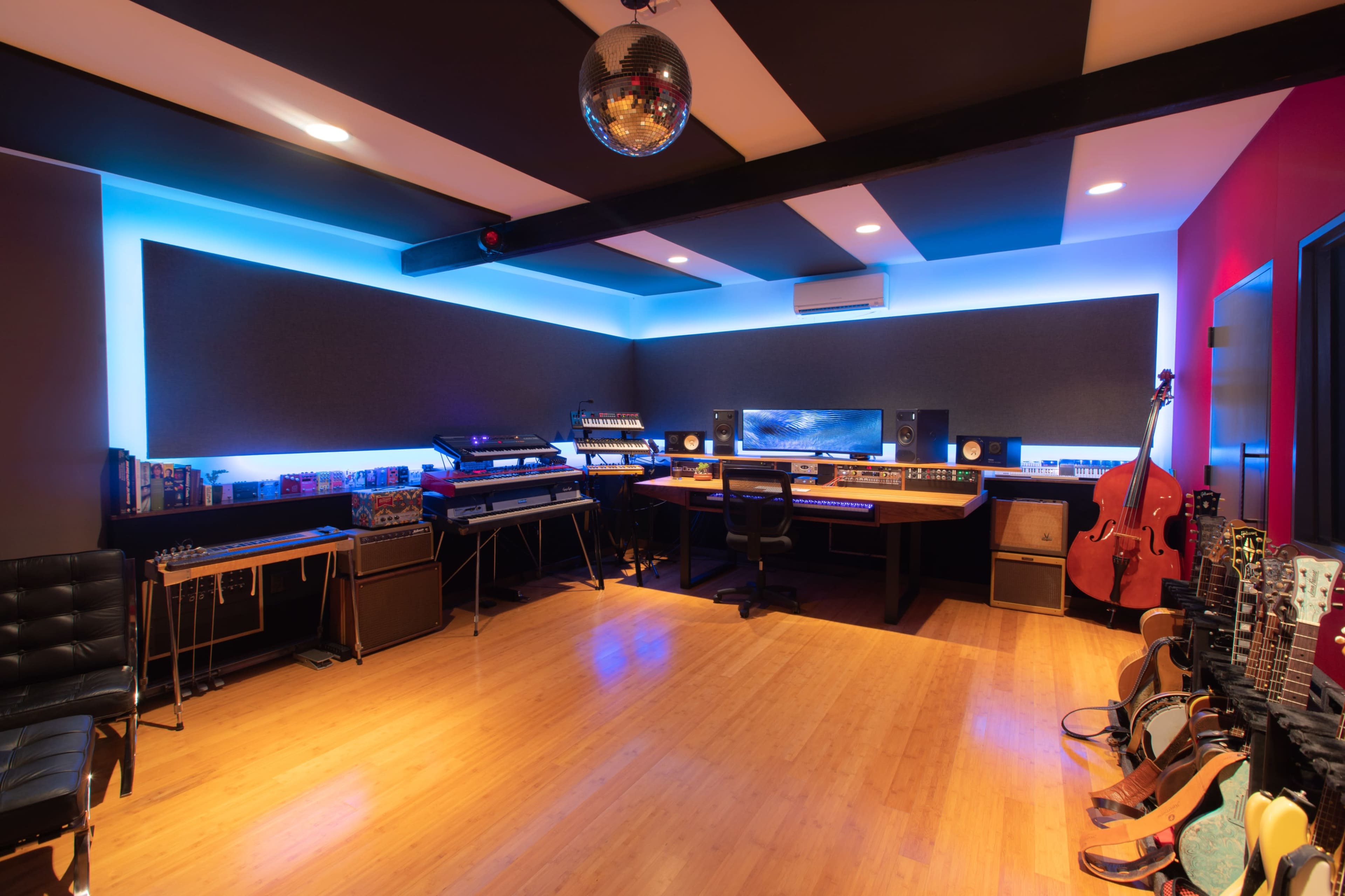 A modern music studio featuring various electronic instruments, acoustic panels, a central mixing desk, and ambient lighting.