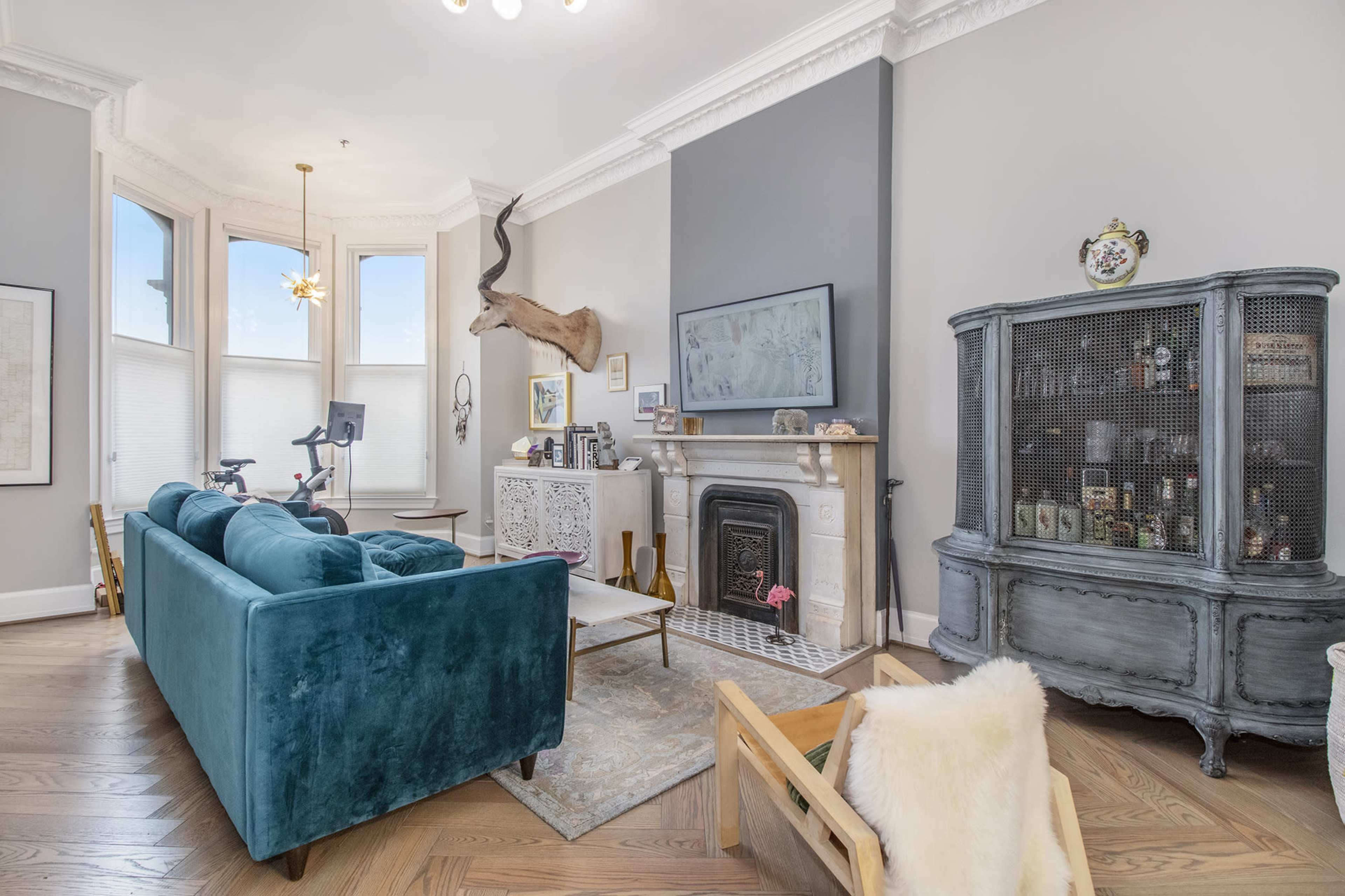 The living room features a teal sofa, a mounted deer head on the wall, a vintage cabinet, and a fireplace surrounded by decorative items.