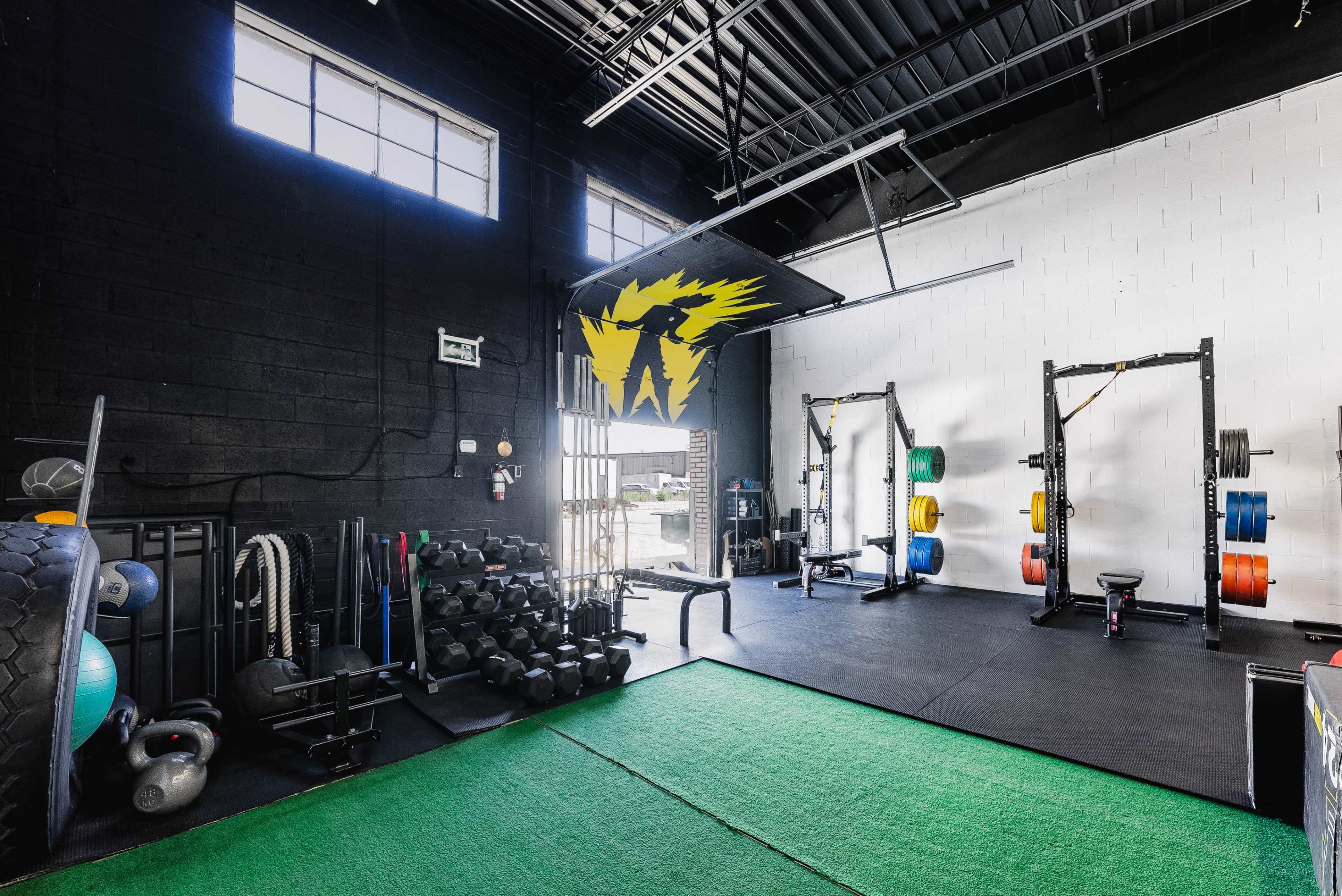 A gym interior with various weightlifting equipment, dumbbells, and exercise mats on a green floor.