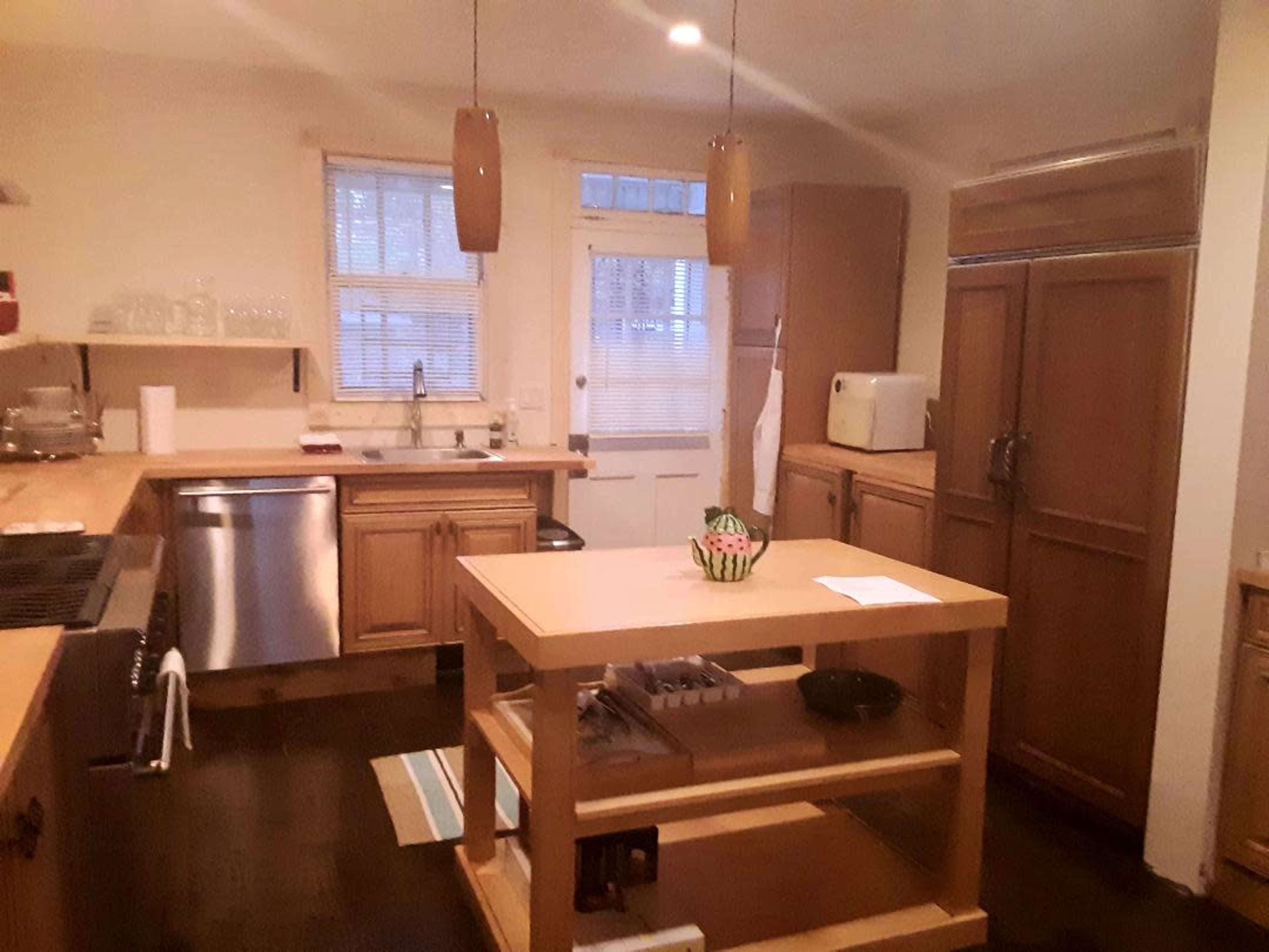 A kitchen with wooden cabinets, a stainless steel refrigerator, a central island, and a door leading to the outside.
