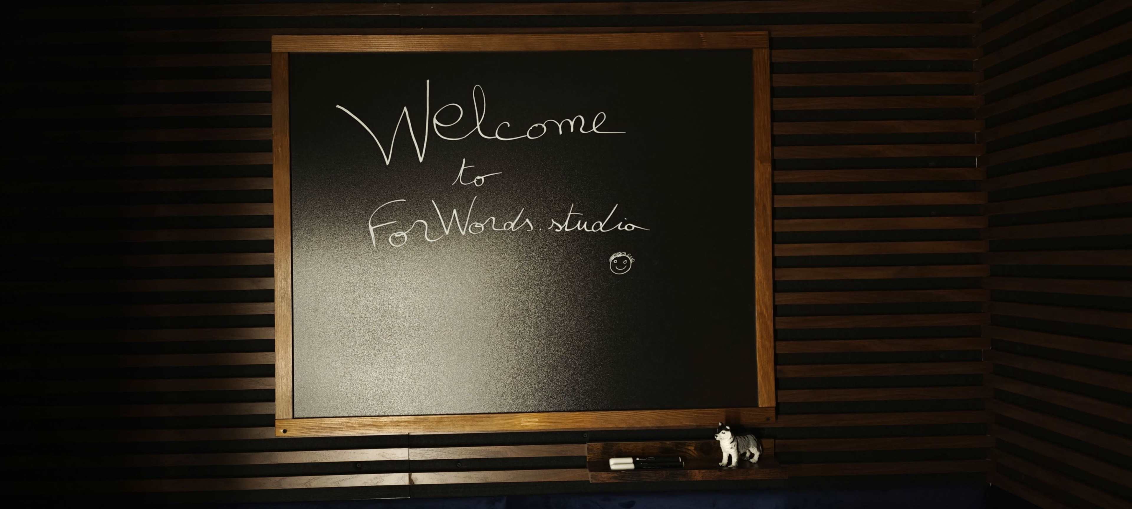 A black chalkboard is framed in wood, displaying a welcome message for "ForWords studio."