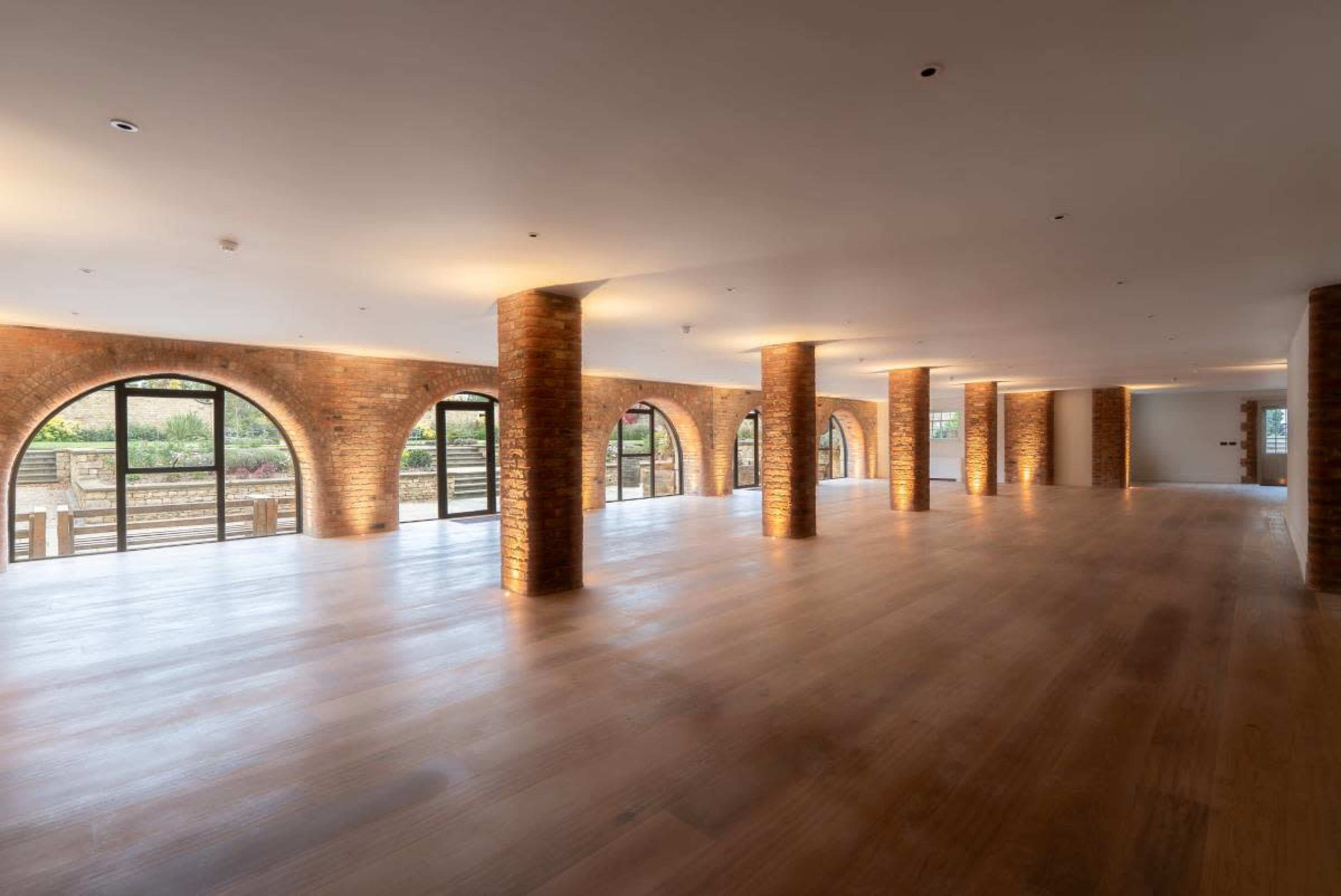 The image shows a spacious interior with arched brick columns and large windows overlooking an outdoor area.