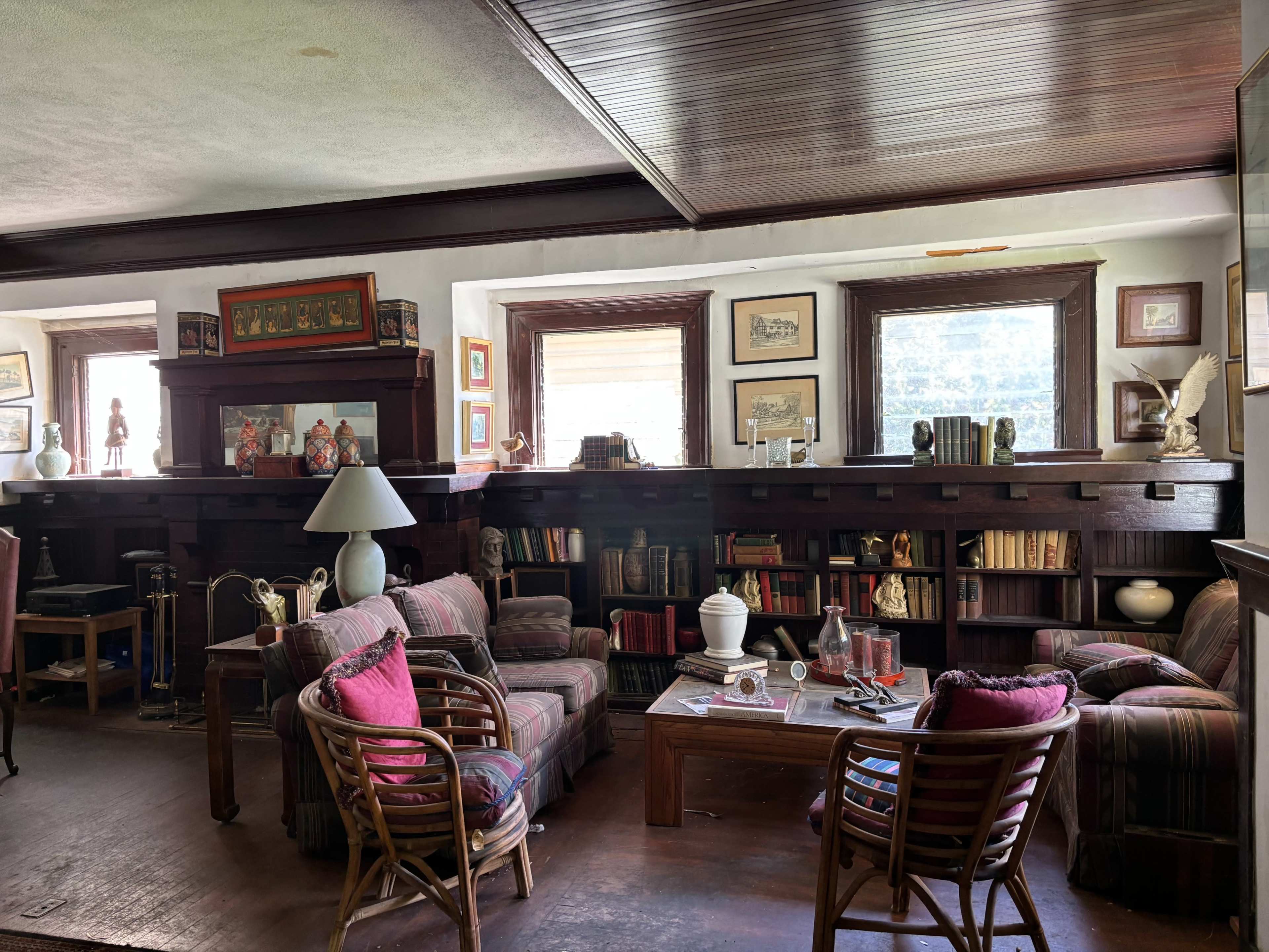 The image depicts a cozy living room with a mixture of armchairs, sofas, and bookshelves filled with books and decorative items.