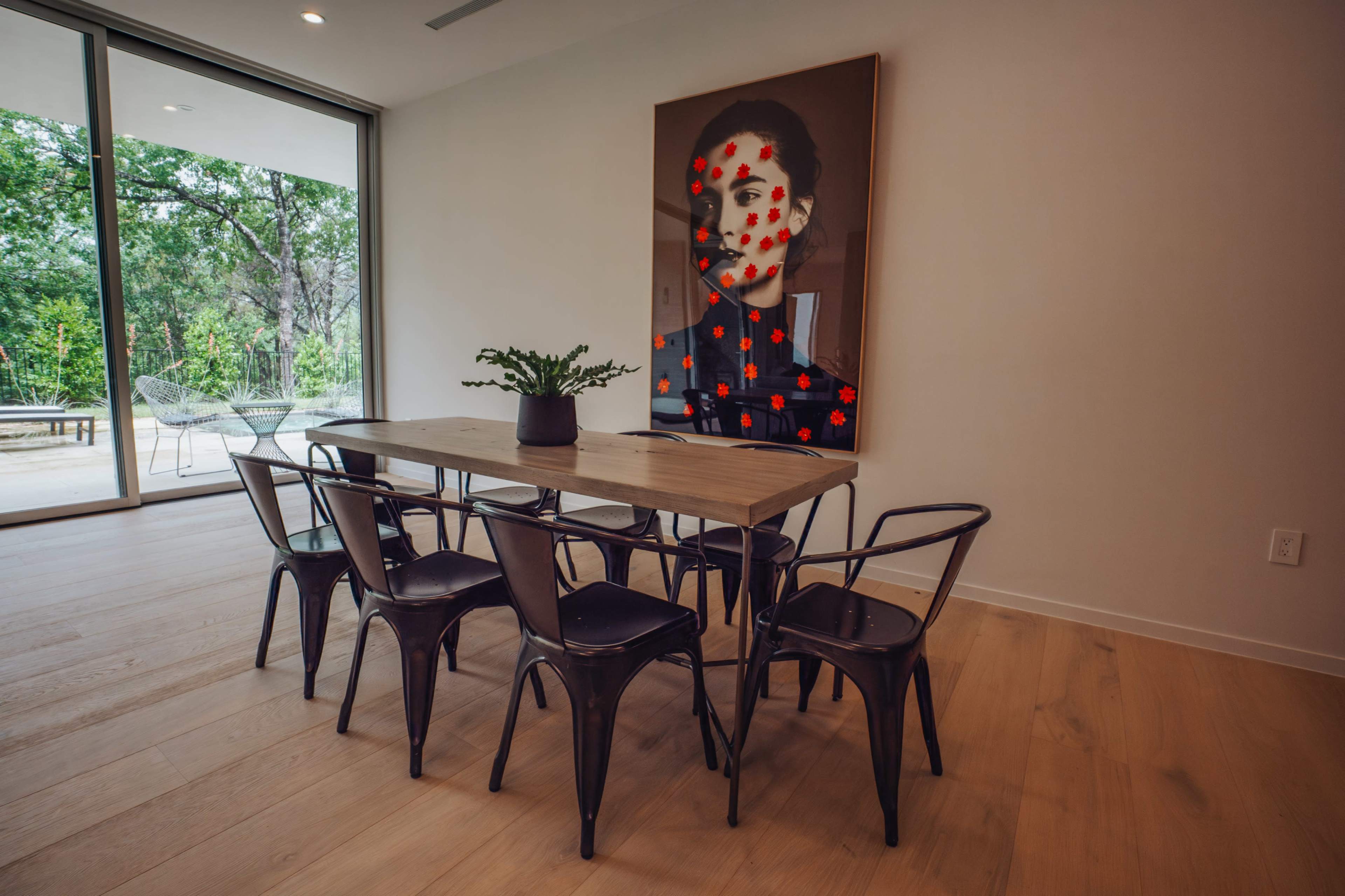 A modern dining area features a wooden table surrounded by six black chairs, with a large portrait displaying red dots hanging on the wall.