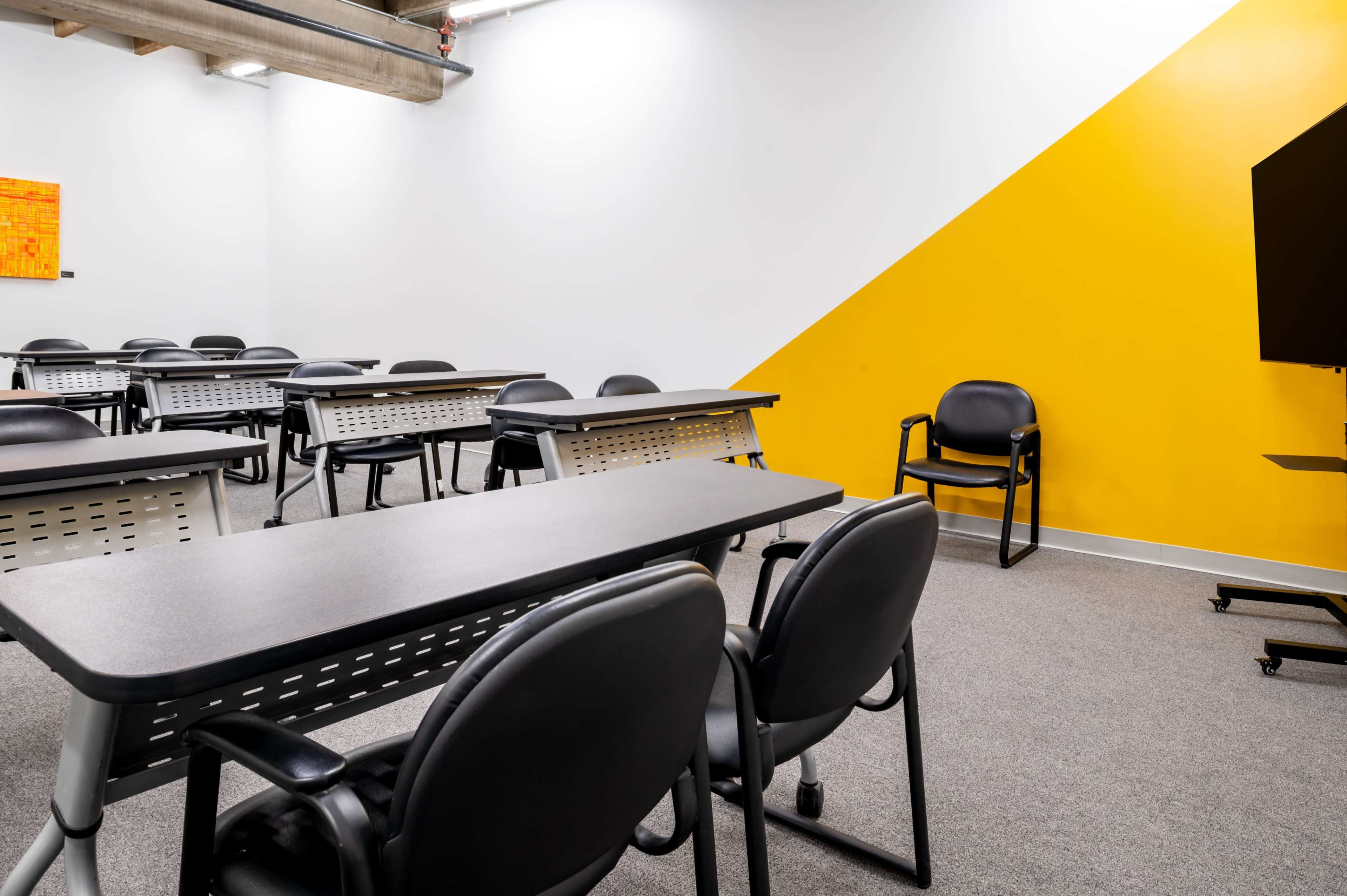 A classroom setup features rows of tables and chairs, set against a wall with a bold yellow triangle design.