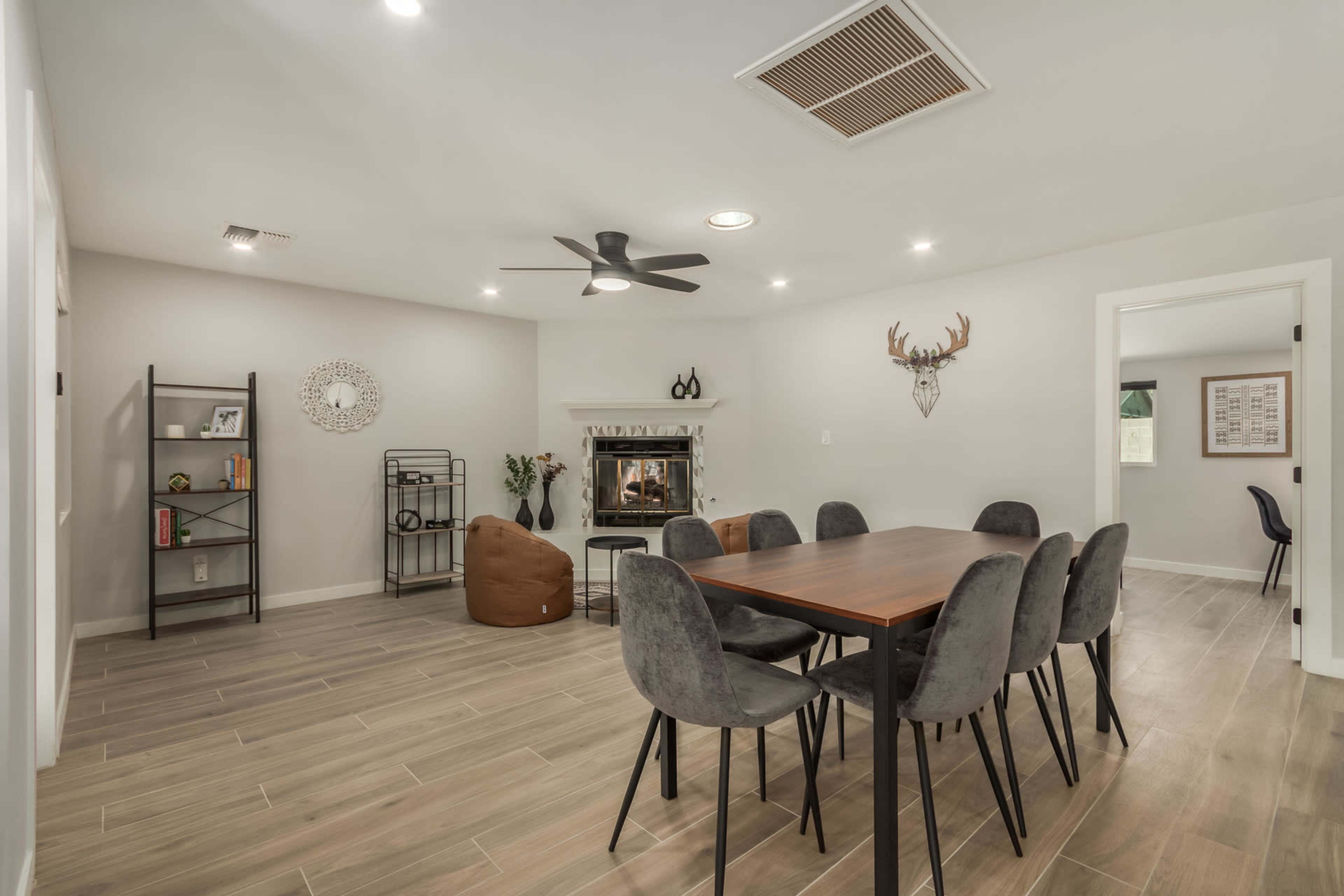 A modern living space features a dining table with six chairs, a fireplace, and various decorative elements against light-colored walls.