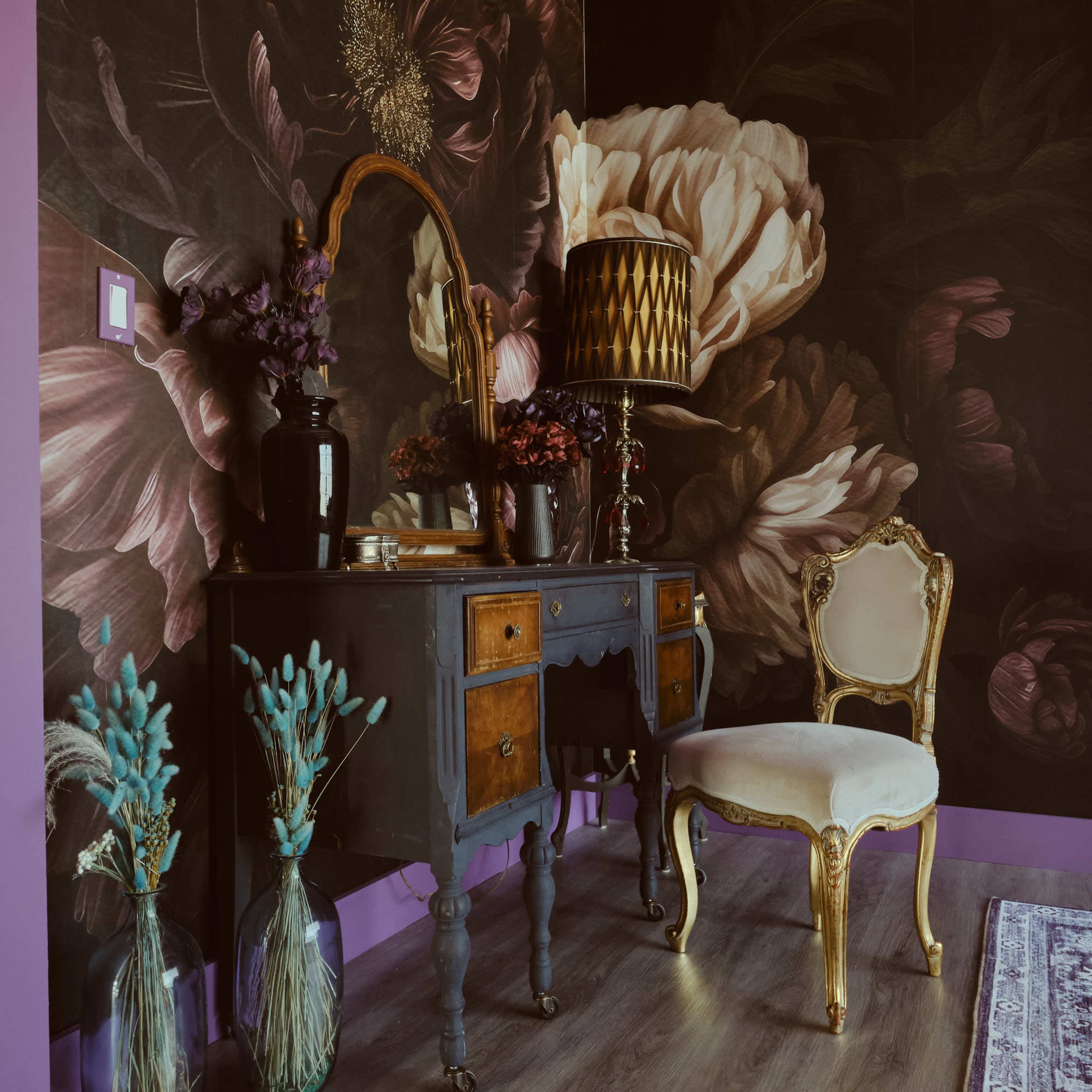 The image depicts a vintage vanity table with a mirror and a luxurious gold-accented chair, set against a floral wallpaper and complemented by decorative vases and a lamp.