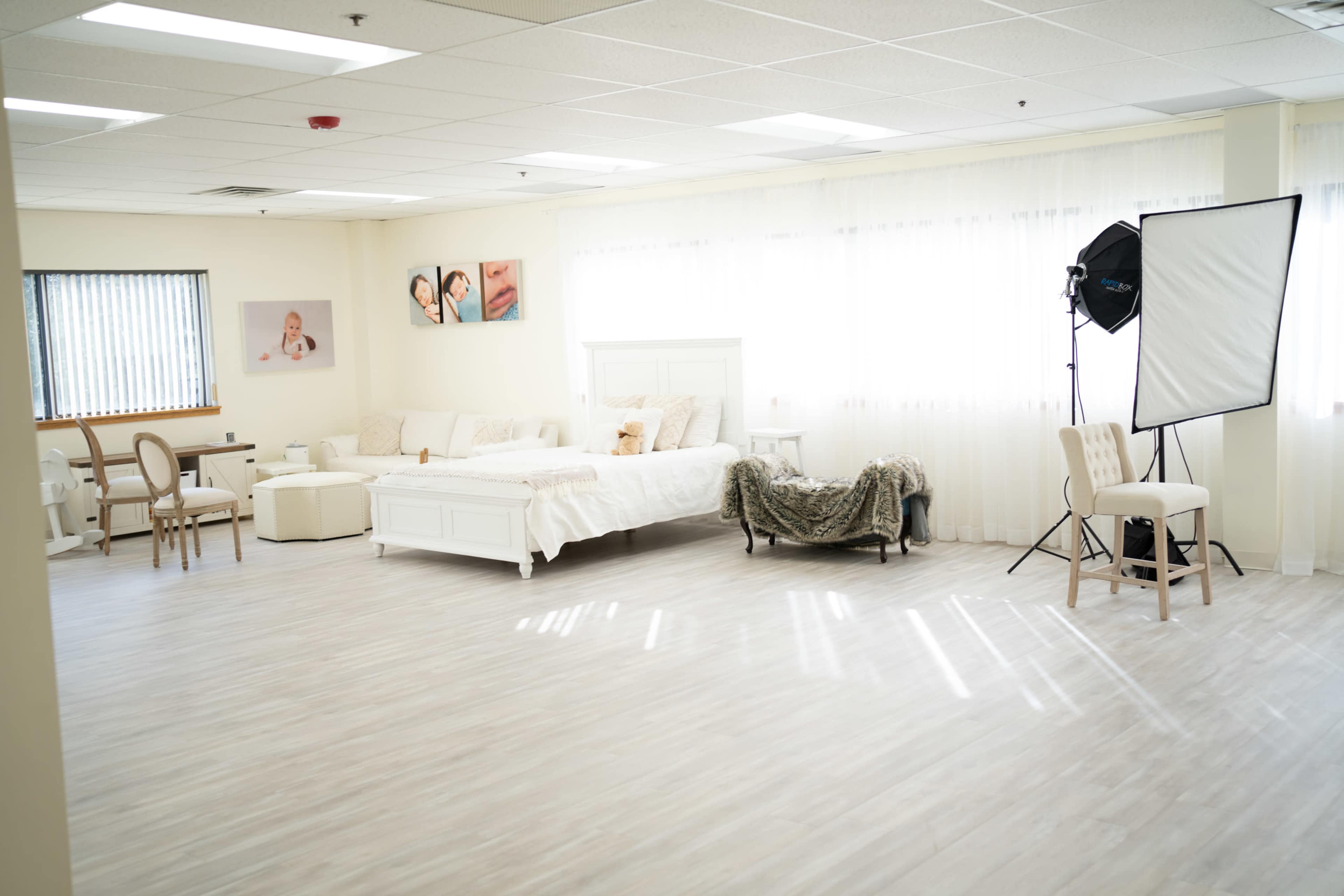 A bright, spacious room with a bed, chairs, and photography equipment near large windows.