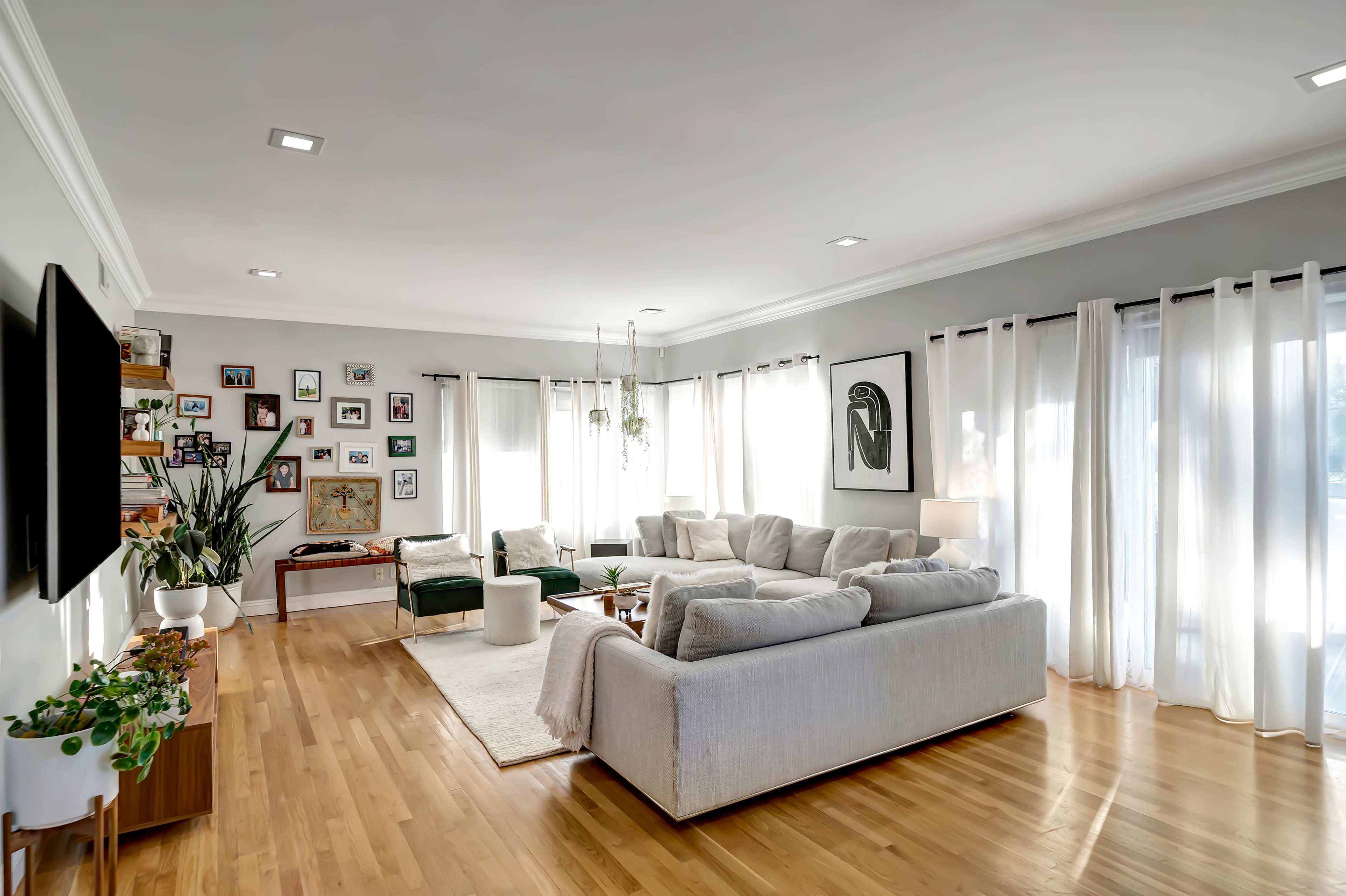 The living room features a large sectional sofa, a coffee table, and a mix of framed photographs on the walls, with natural light streaming through the sheer curtains.