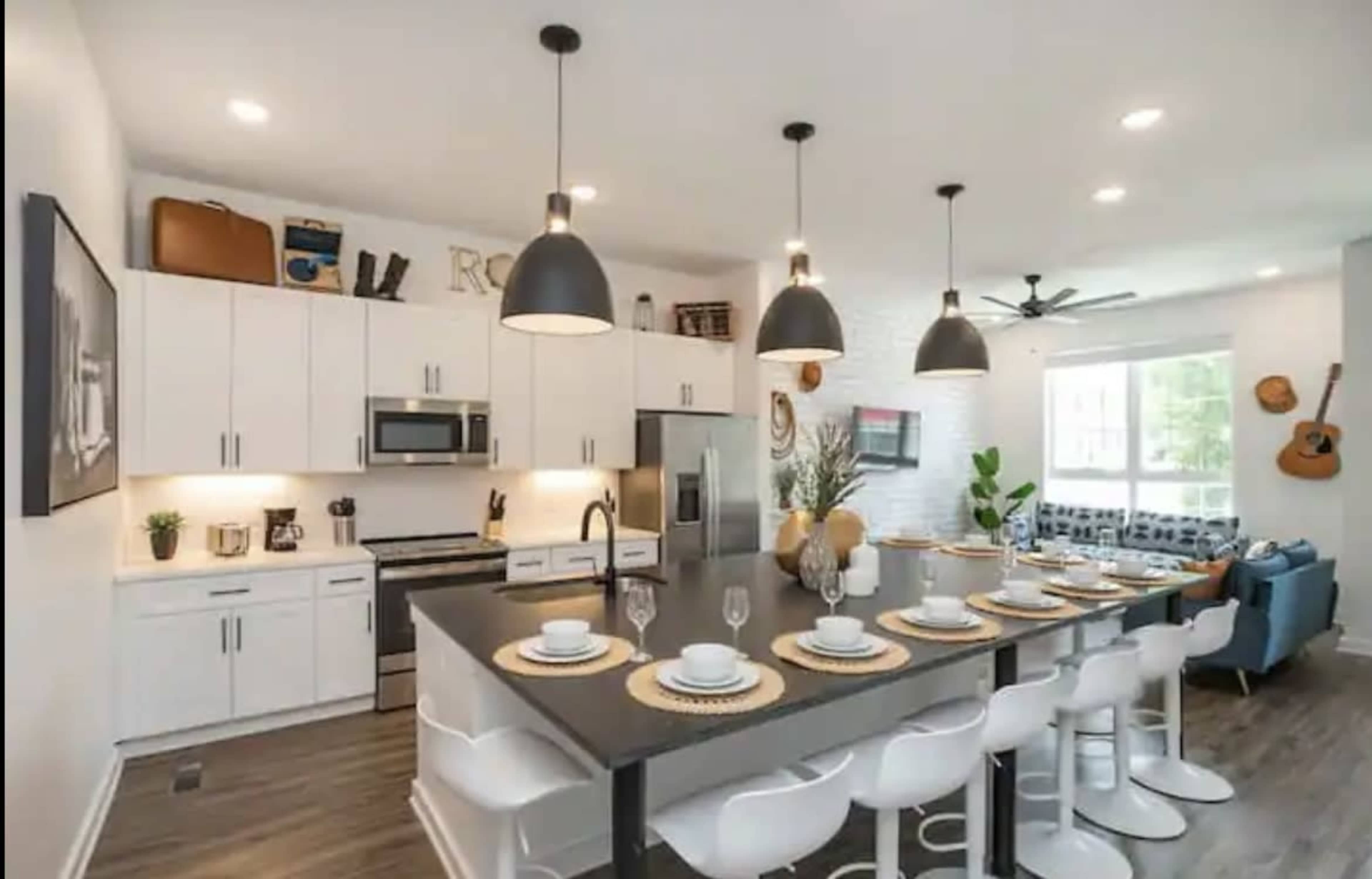 A modern kitchen features white cabinetry, stainless steel appliances, and a large island with seating for eight.