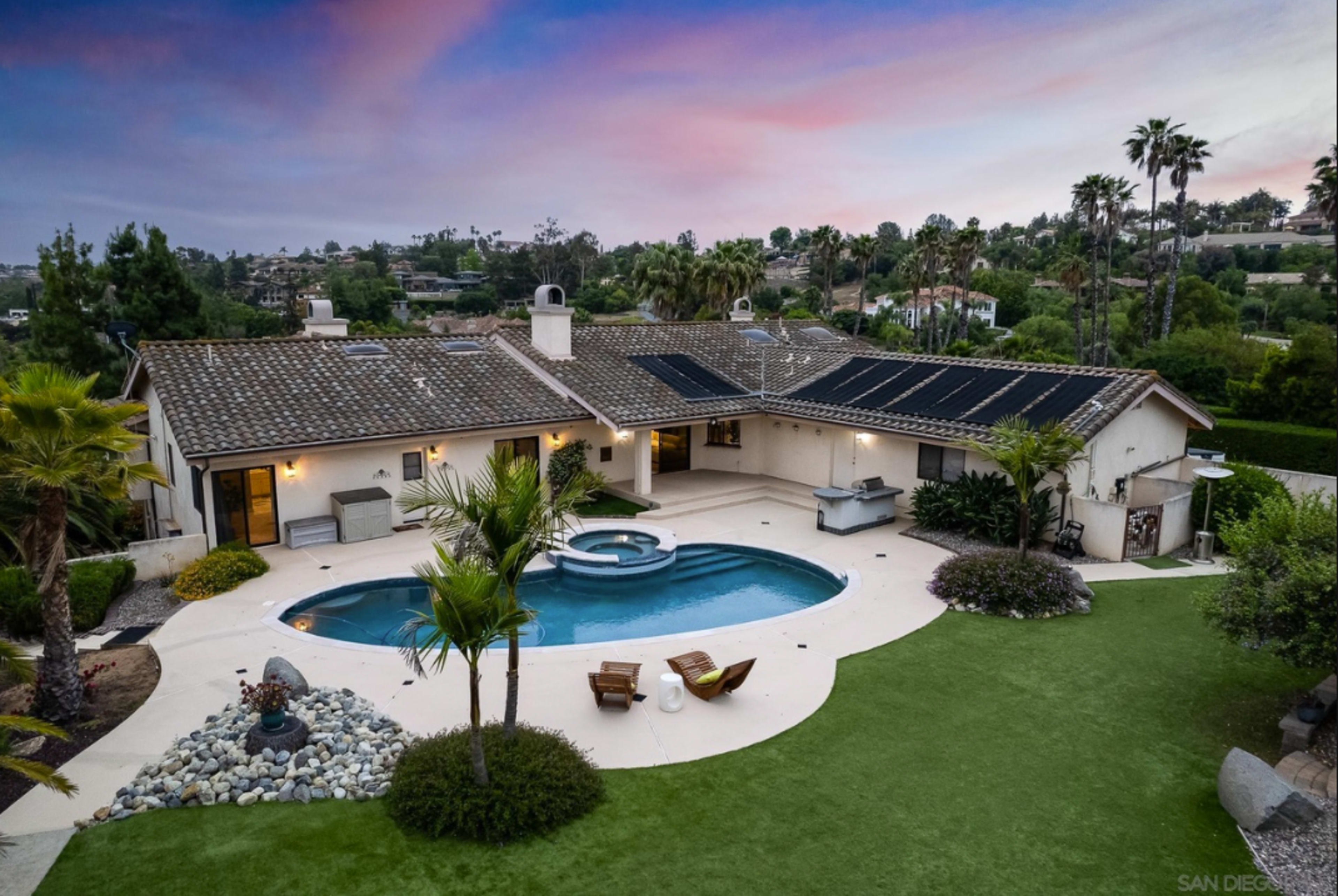 The image shows a suburban house with a swimming pool, palm trees, and a landscaped yard at dusk, featuring a vibrant sky.