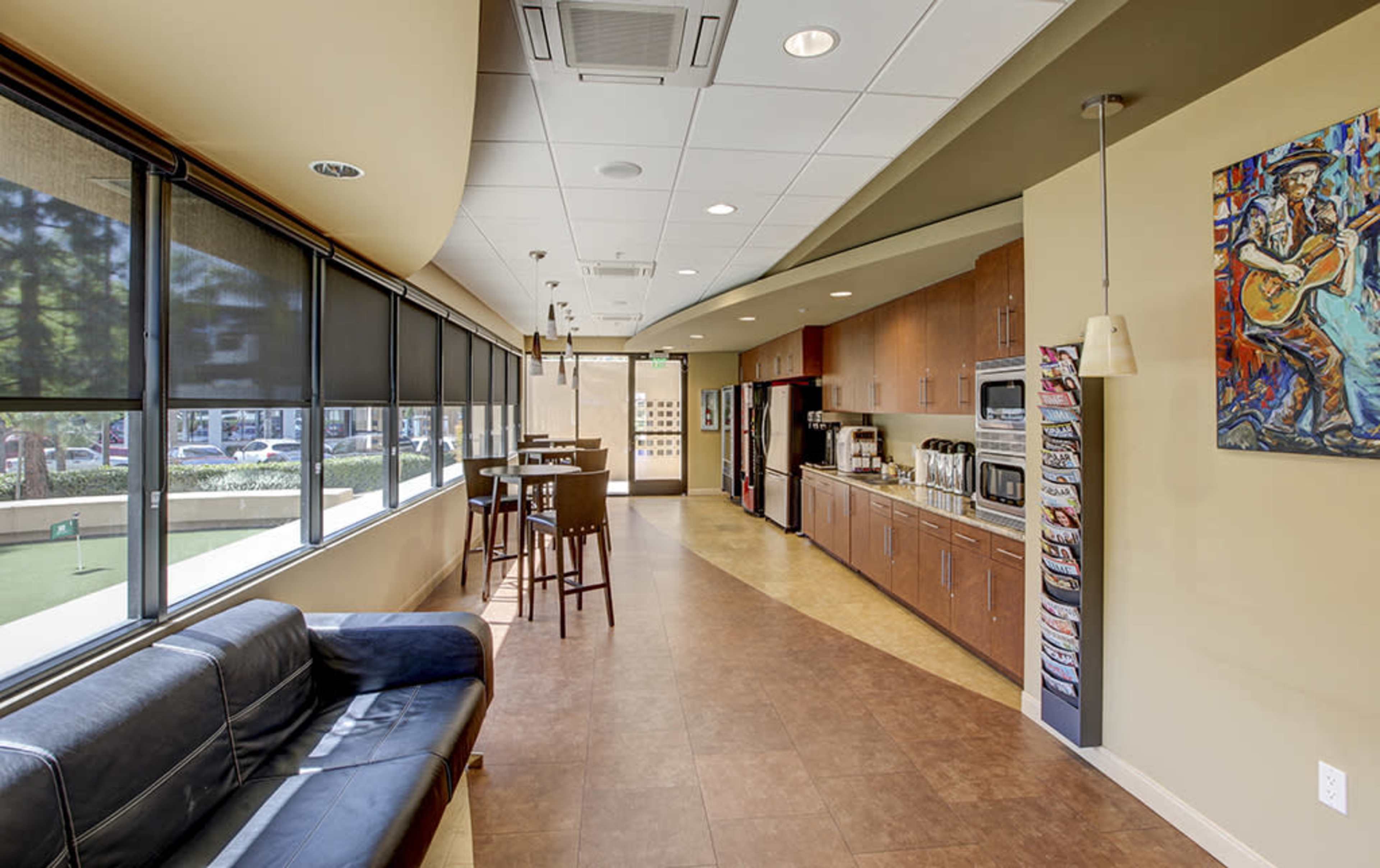A recreational area with a kitchen, seating space, and large windows overlooking a green outdoor area.