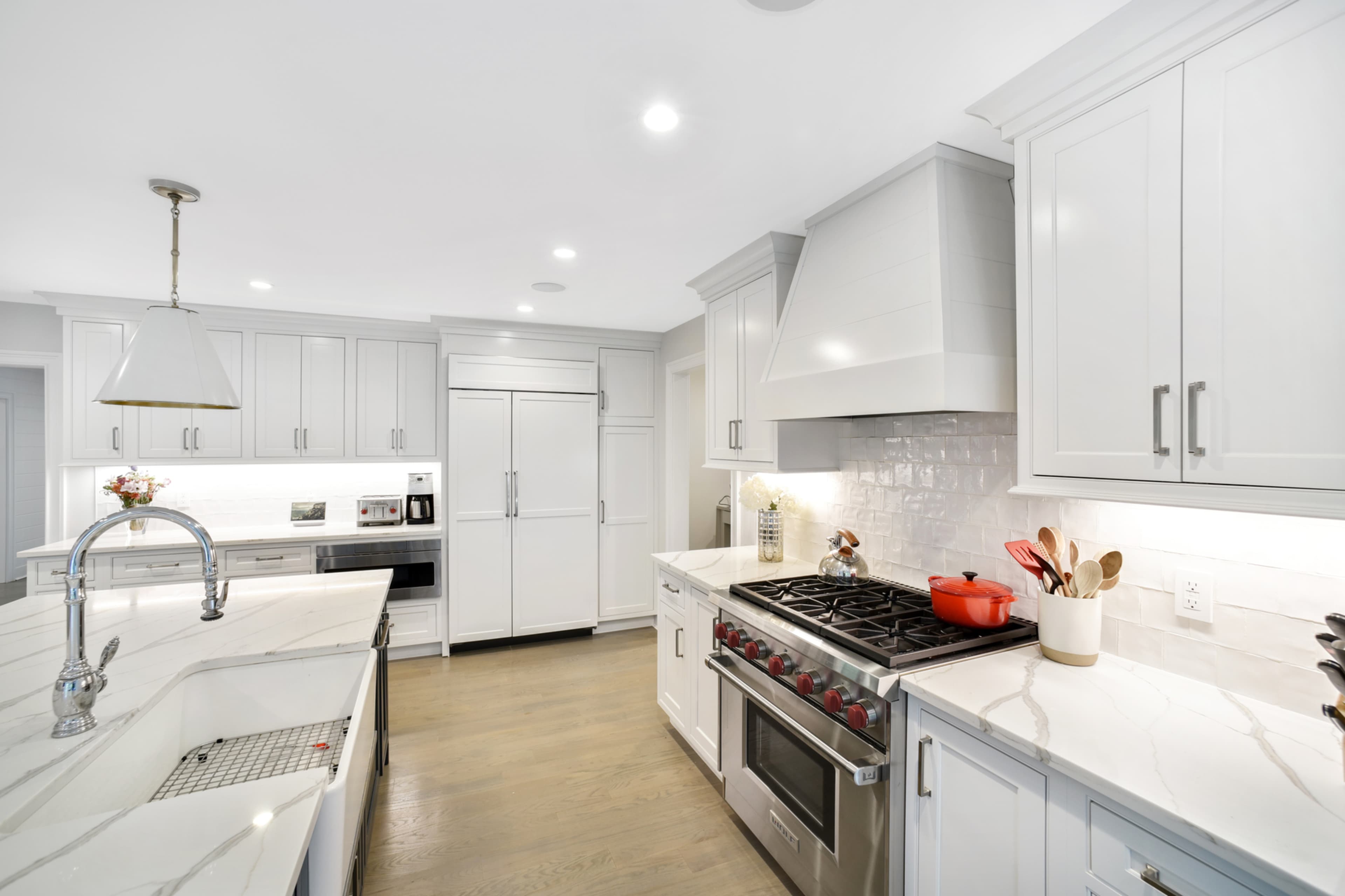 The kitchen features white cabinetry, a large central island with a sink, stainless steel appliances, and a gas range.