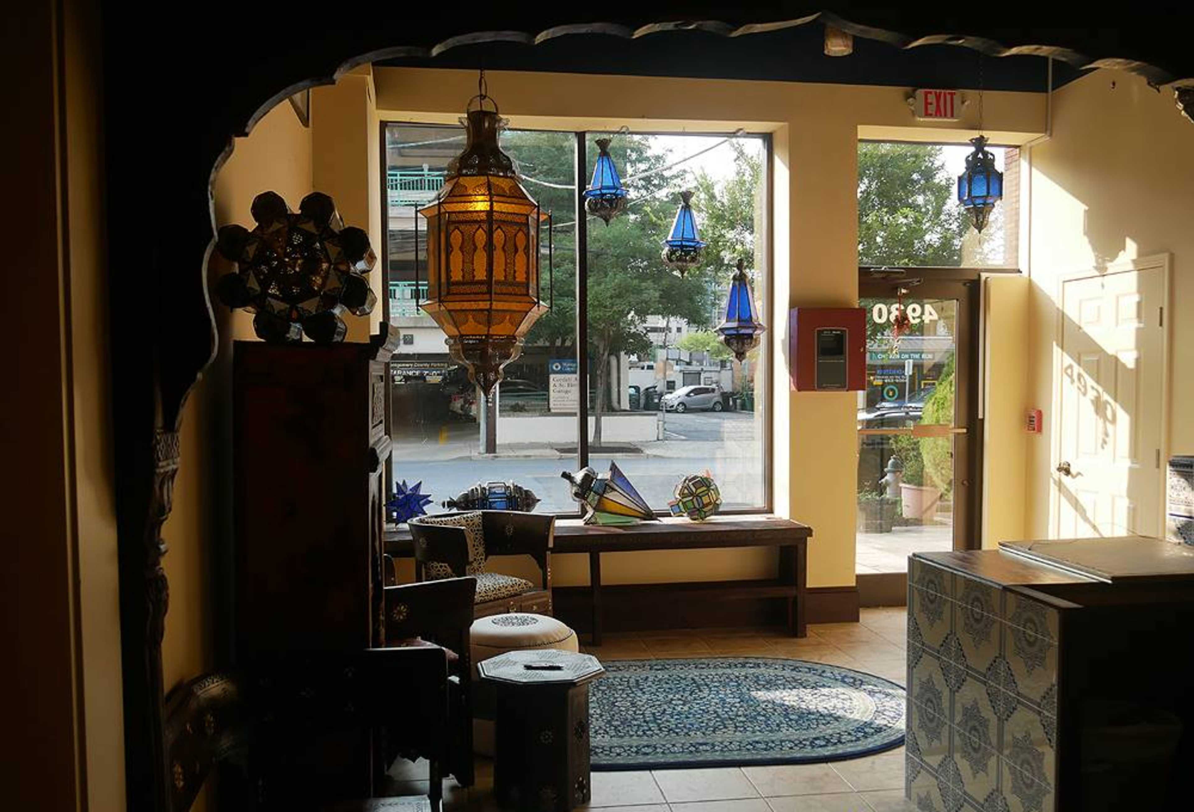 The image shows a brightly lit shop interior with decorative lanterns hanging from the ceiling and various crafted items displayed on benches and tables near a large window.
