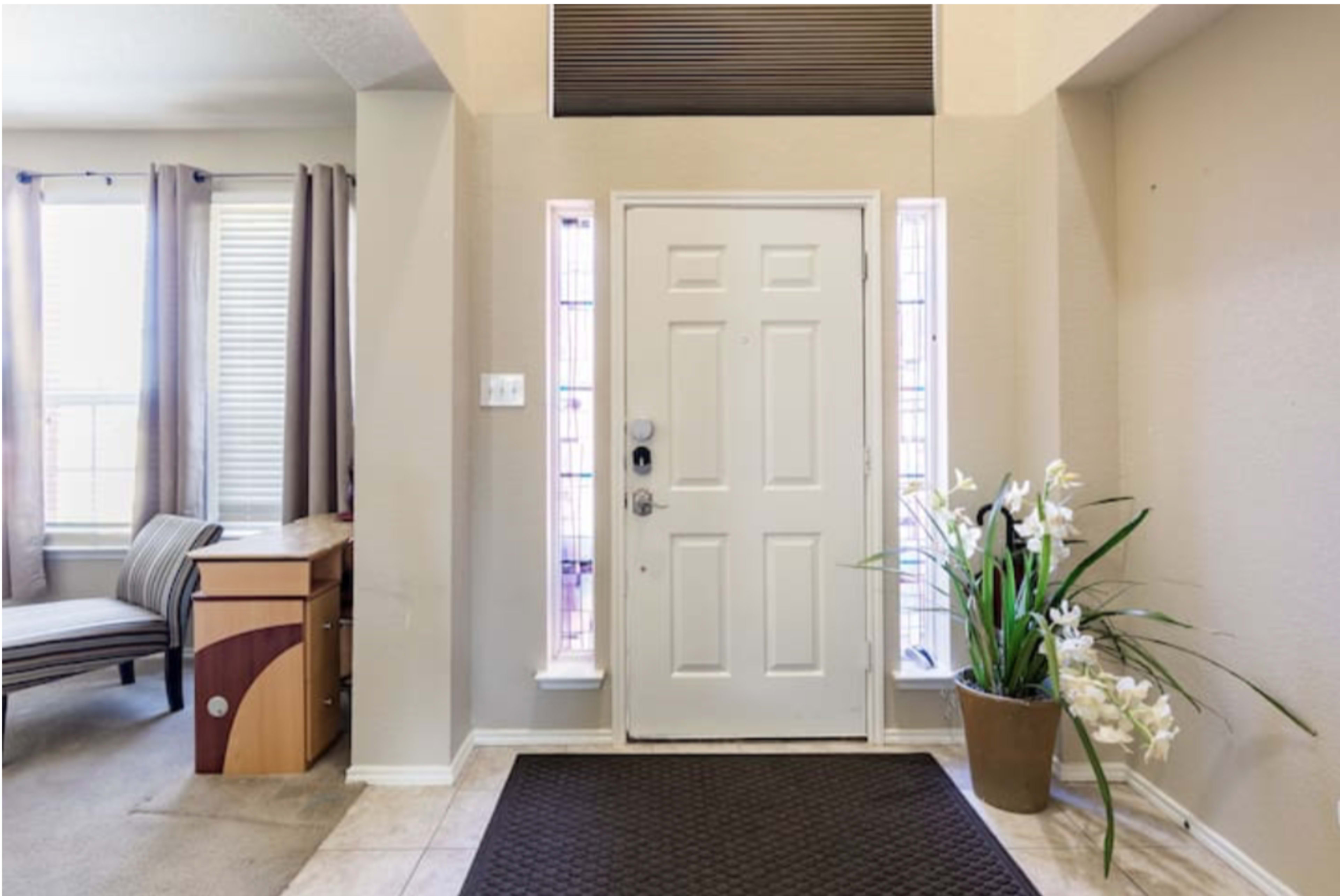 A home's entrance with a white front door, beige walls, a tiled floor, and a potted plant beside the door.