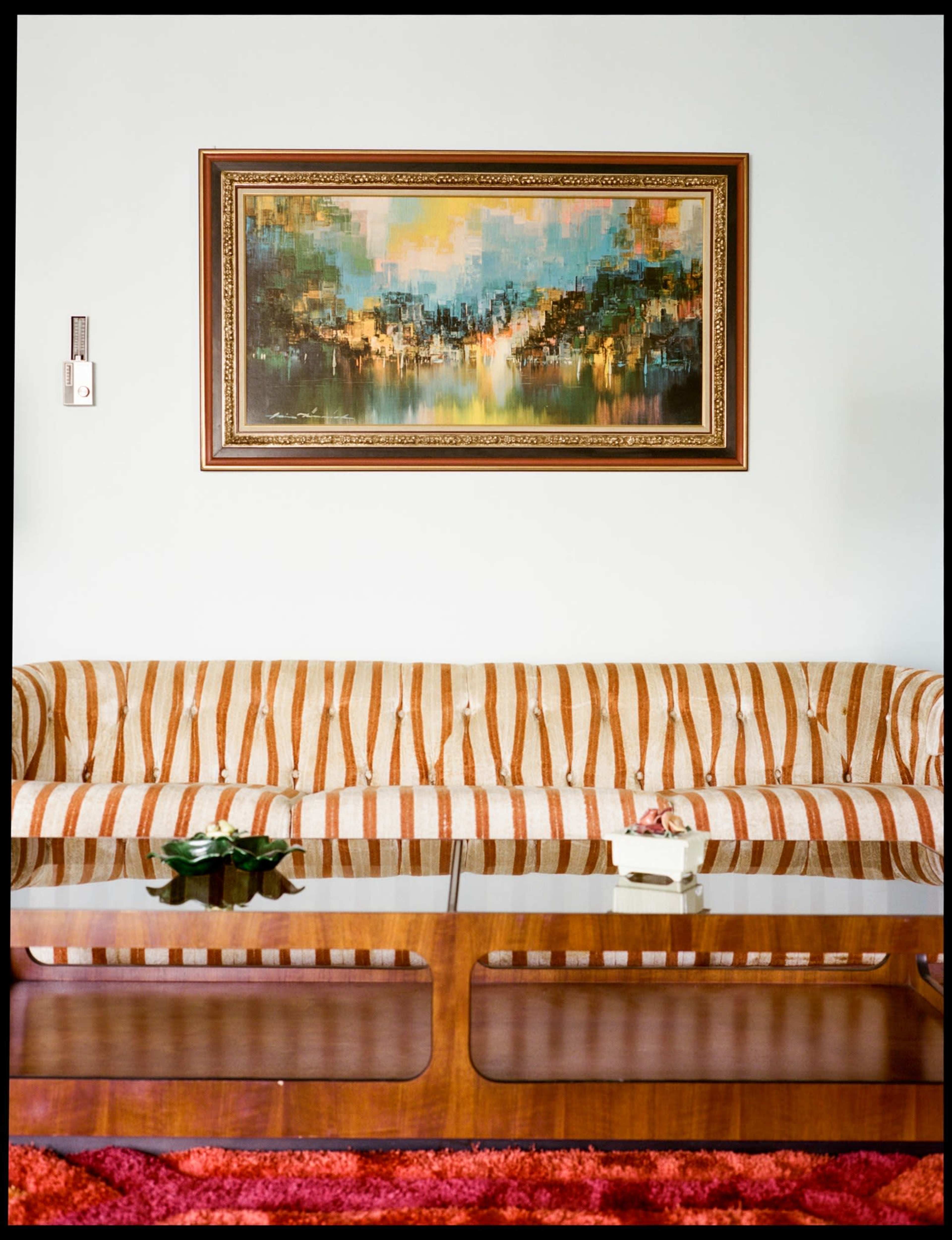 The image shows a living room with a striped sofa, a wooden coffee table, and a large painting hanging on the wall above the sofa.