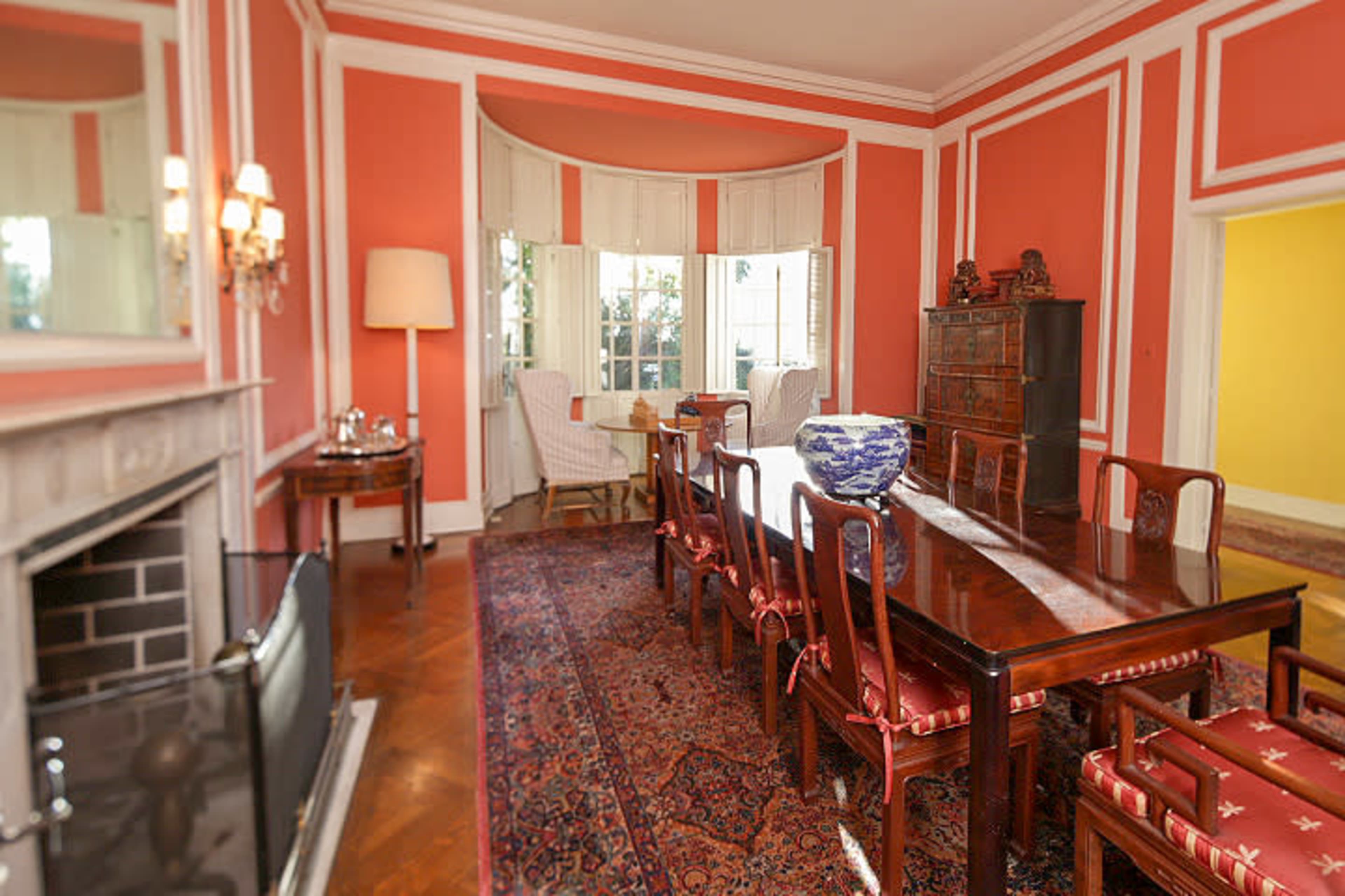 A dining room with a long wooden table surrounded by chairs, decorated with salmon-colored walls and a large window.