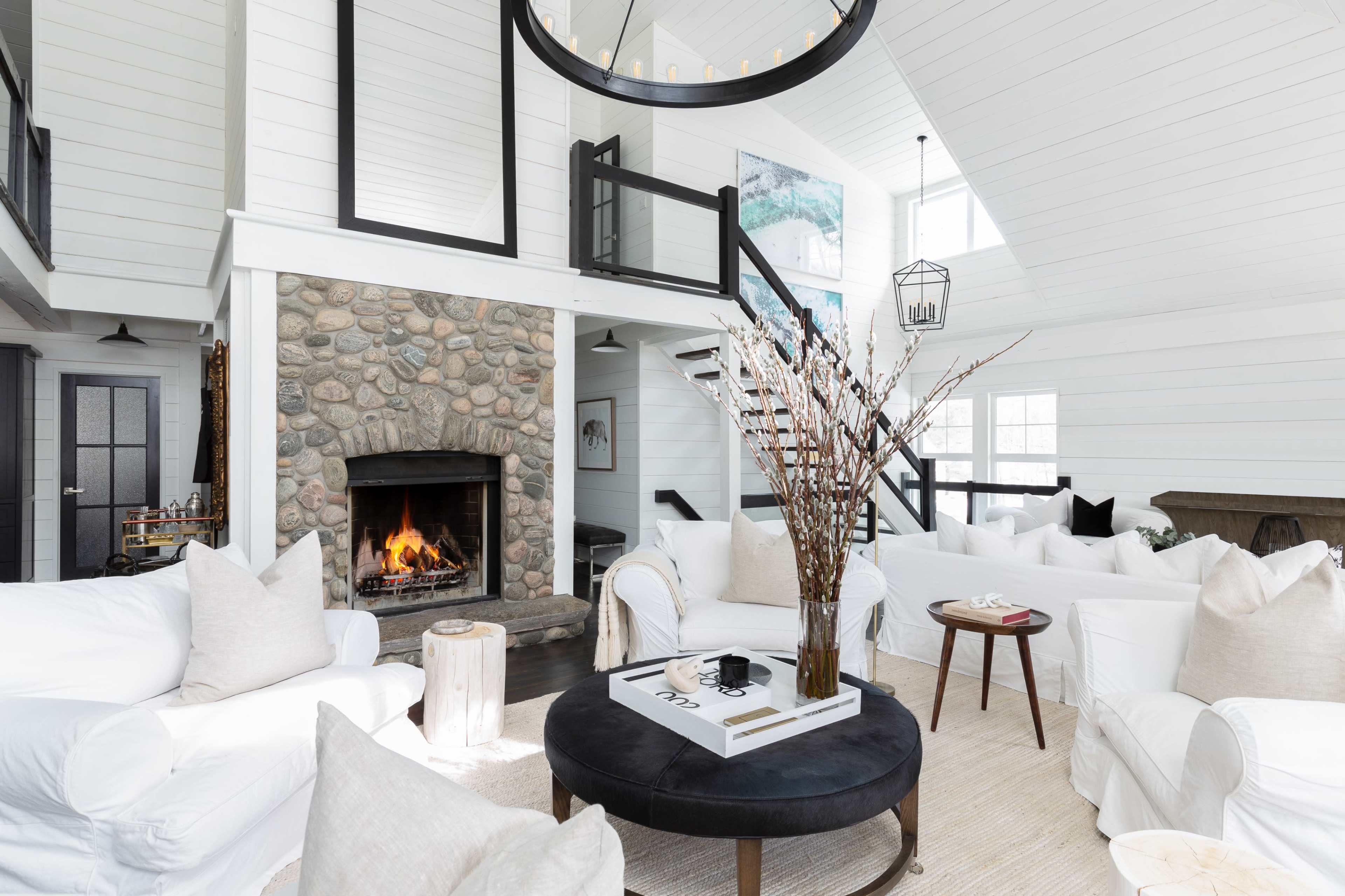 A spacious living room with a stone fireplace, light-colored furniture, and large windows allowing natural light to fill the area.