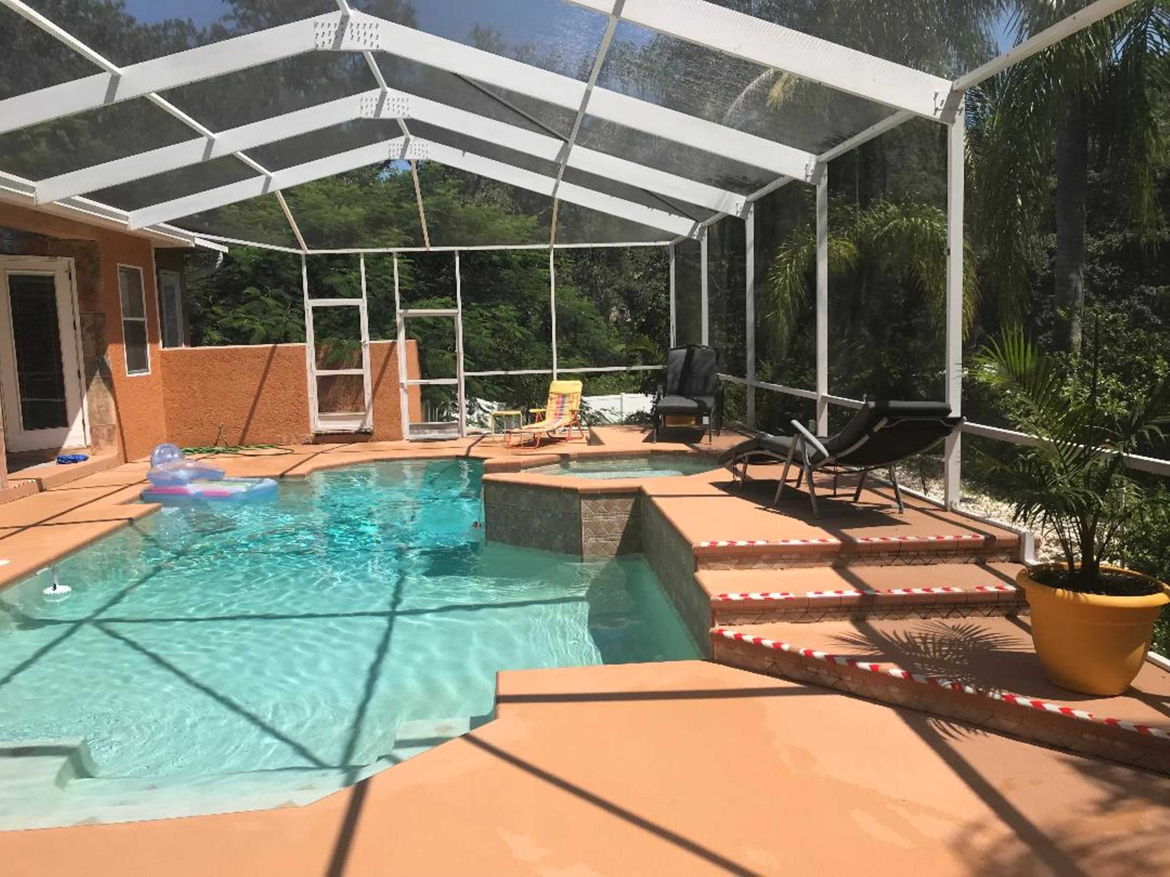 A screened-in pool area with a blue swimming pool, chaise lounges, and surrounding greenery.