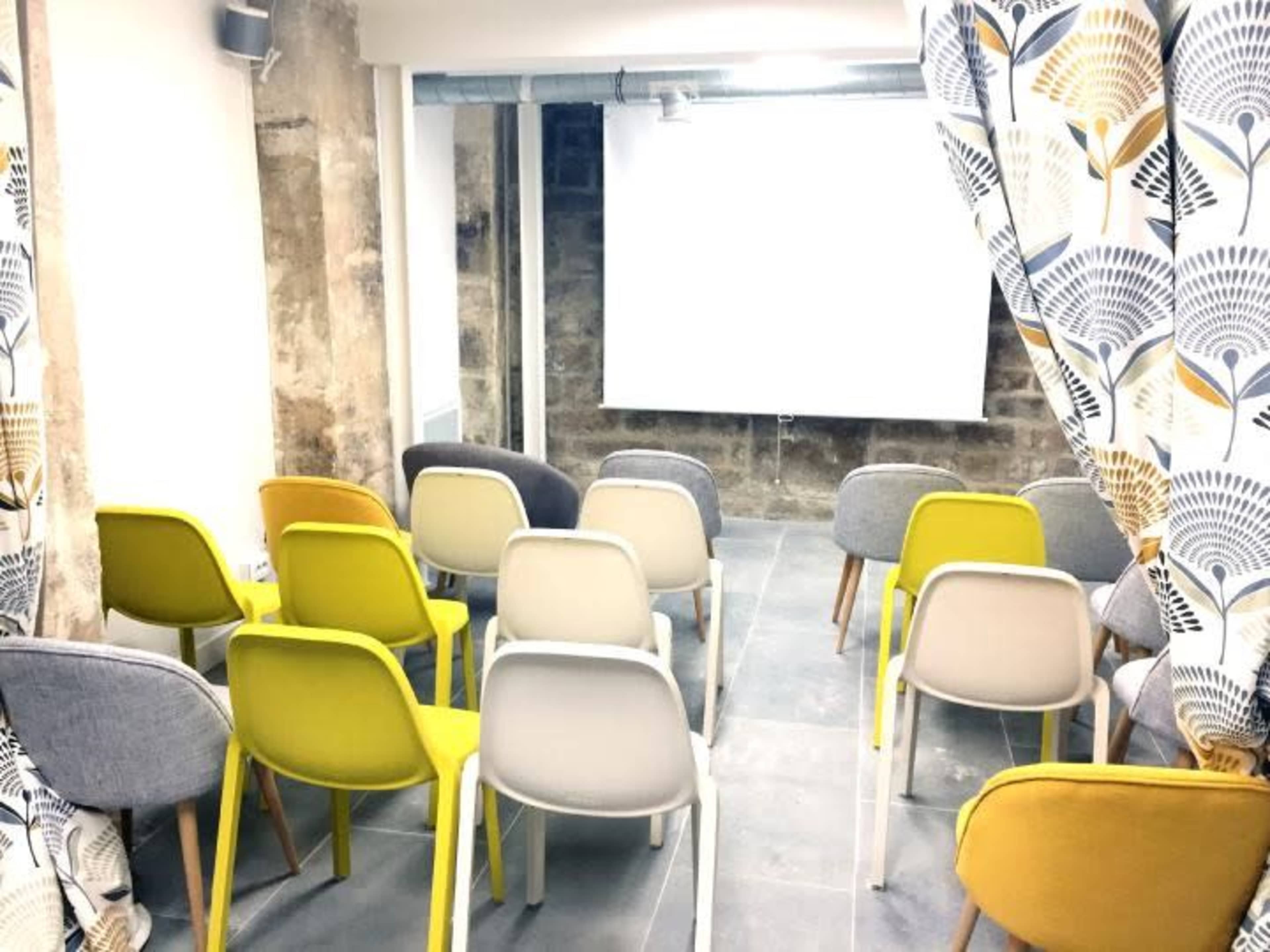 A row of colorful chairs faces a blank projection screen in a modern meeting room.