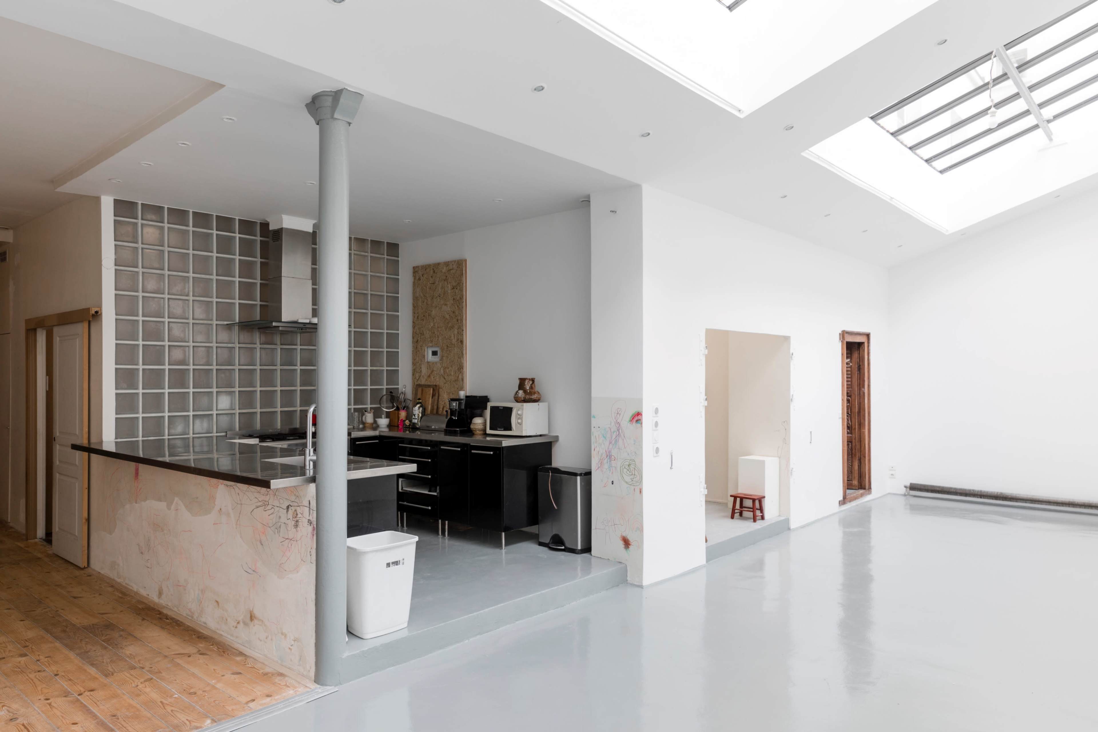 A spacious, modern open-plan kitchen and living area with a sleek countertop, glass blocks, and large skylights.