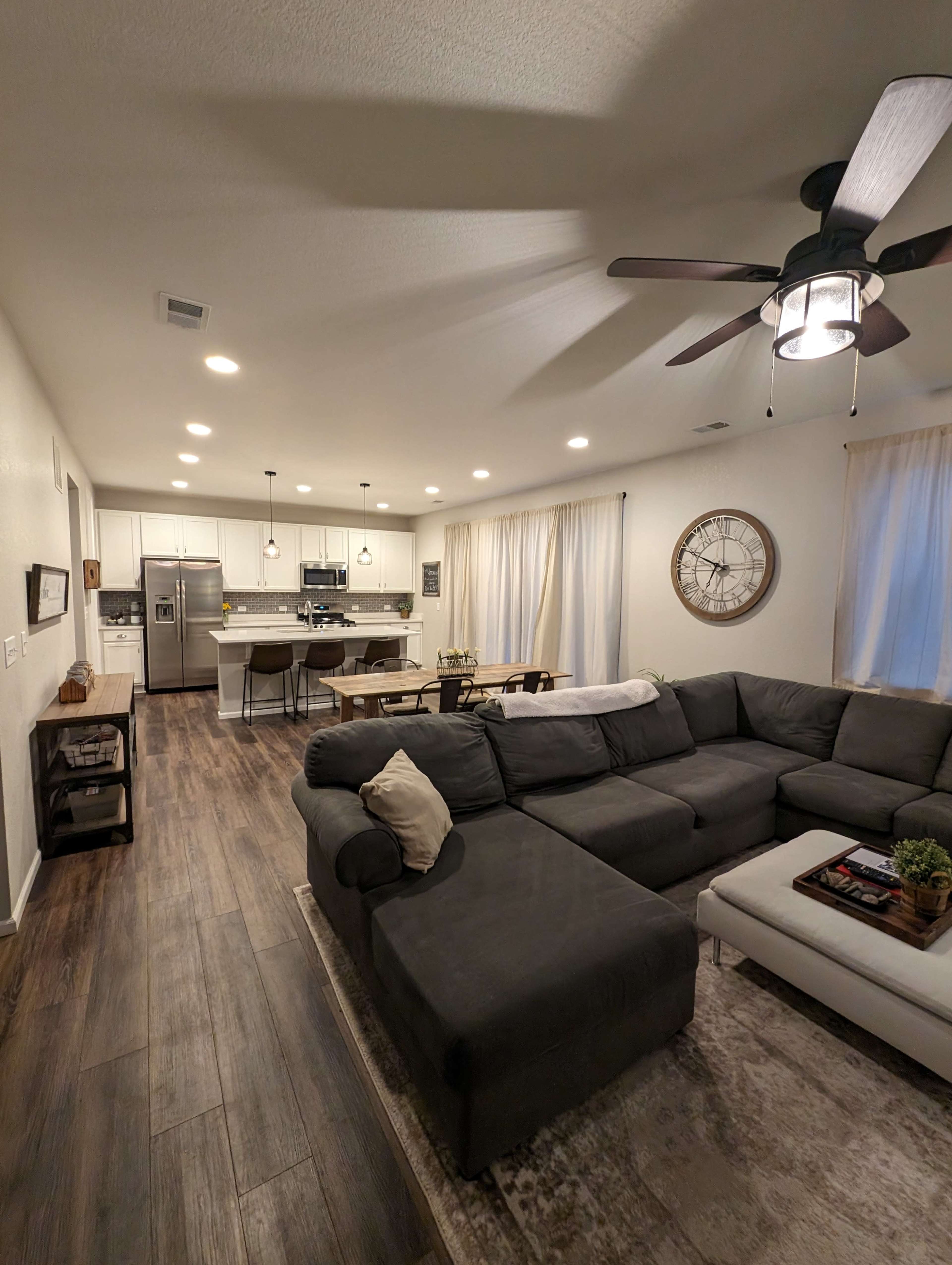 A modern living room with a sectional sofa, a coffee table, and a view of a kitchen area featuring bar stools and white cabinetry.