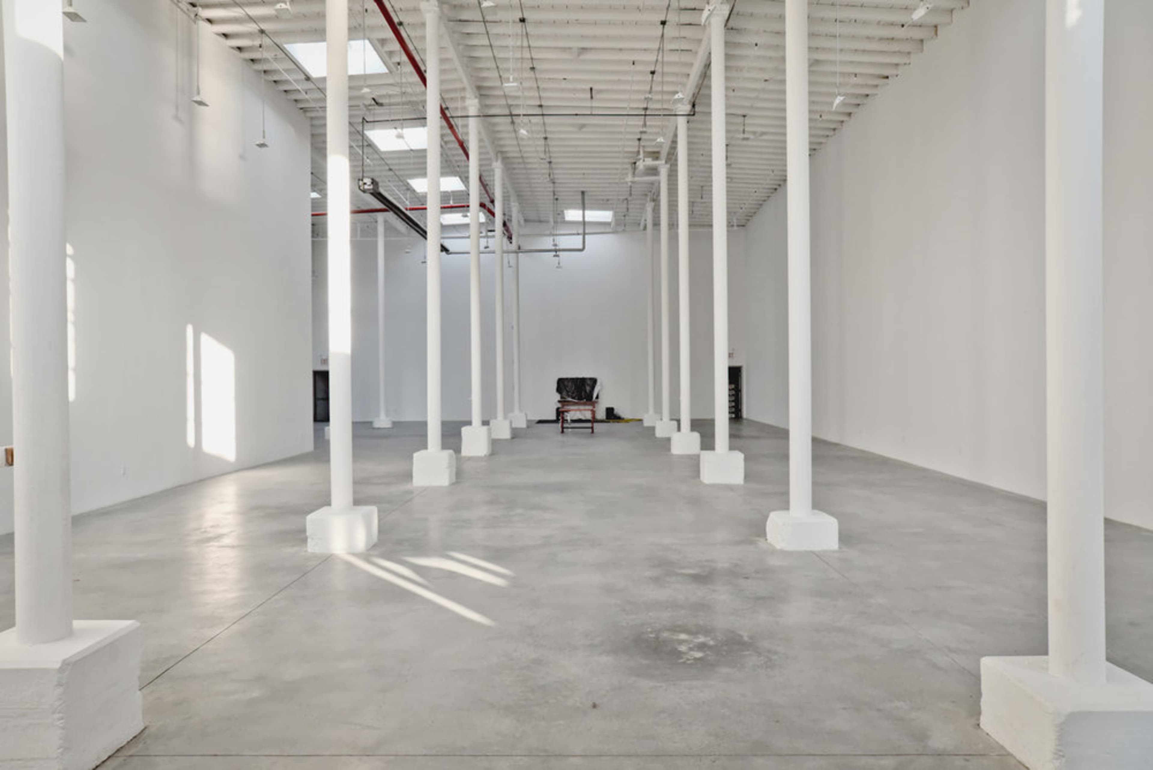 A large, empty room with white walls, a concrete floor, and several white columns supporting the ceiling.