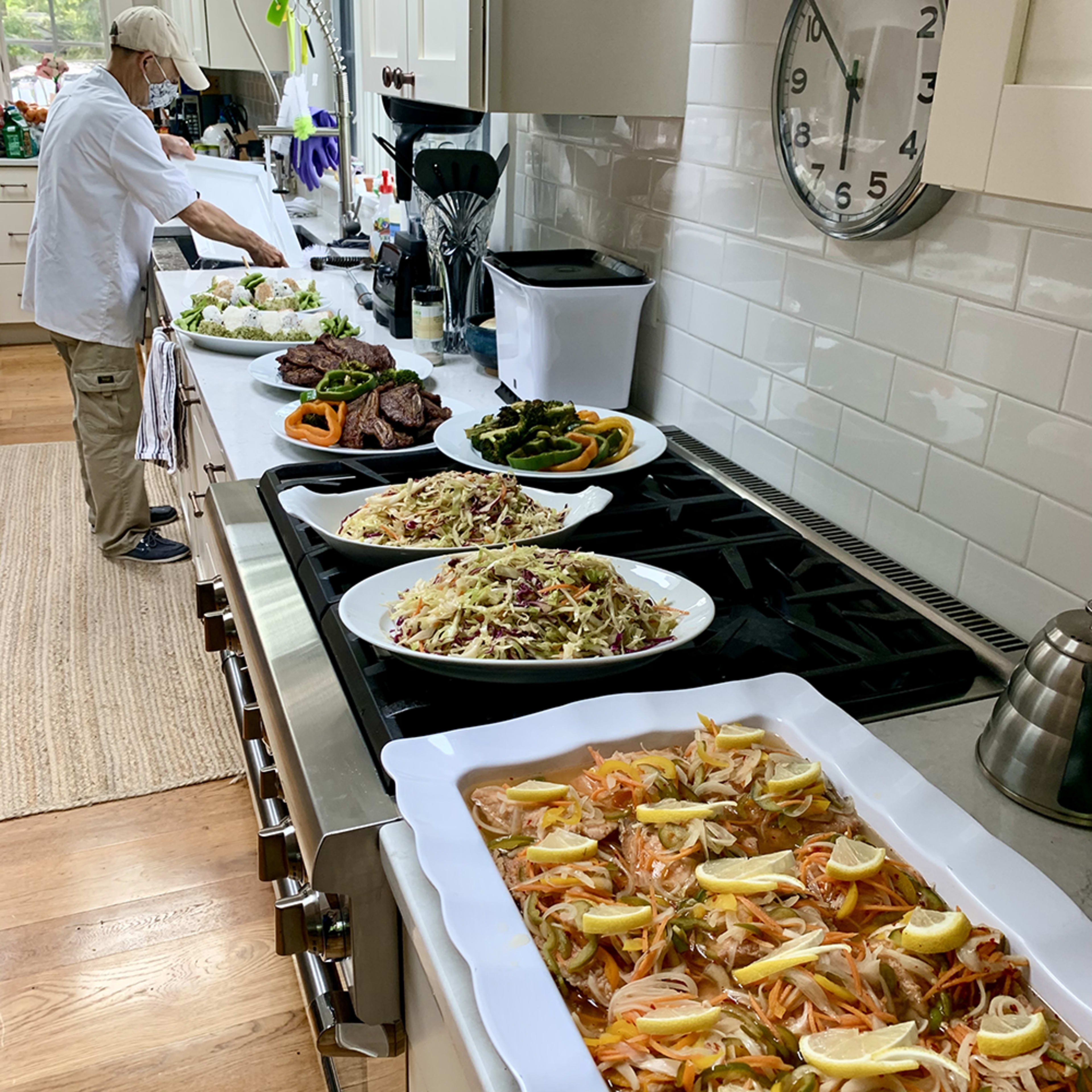A chef prepares food in a kitchen with several dishes, including salads, grilled meat, and vegetables, displayed on the countertop.