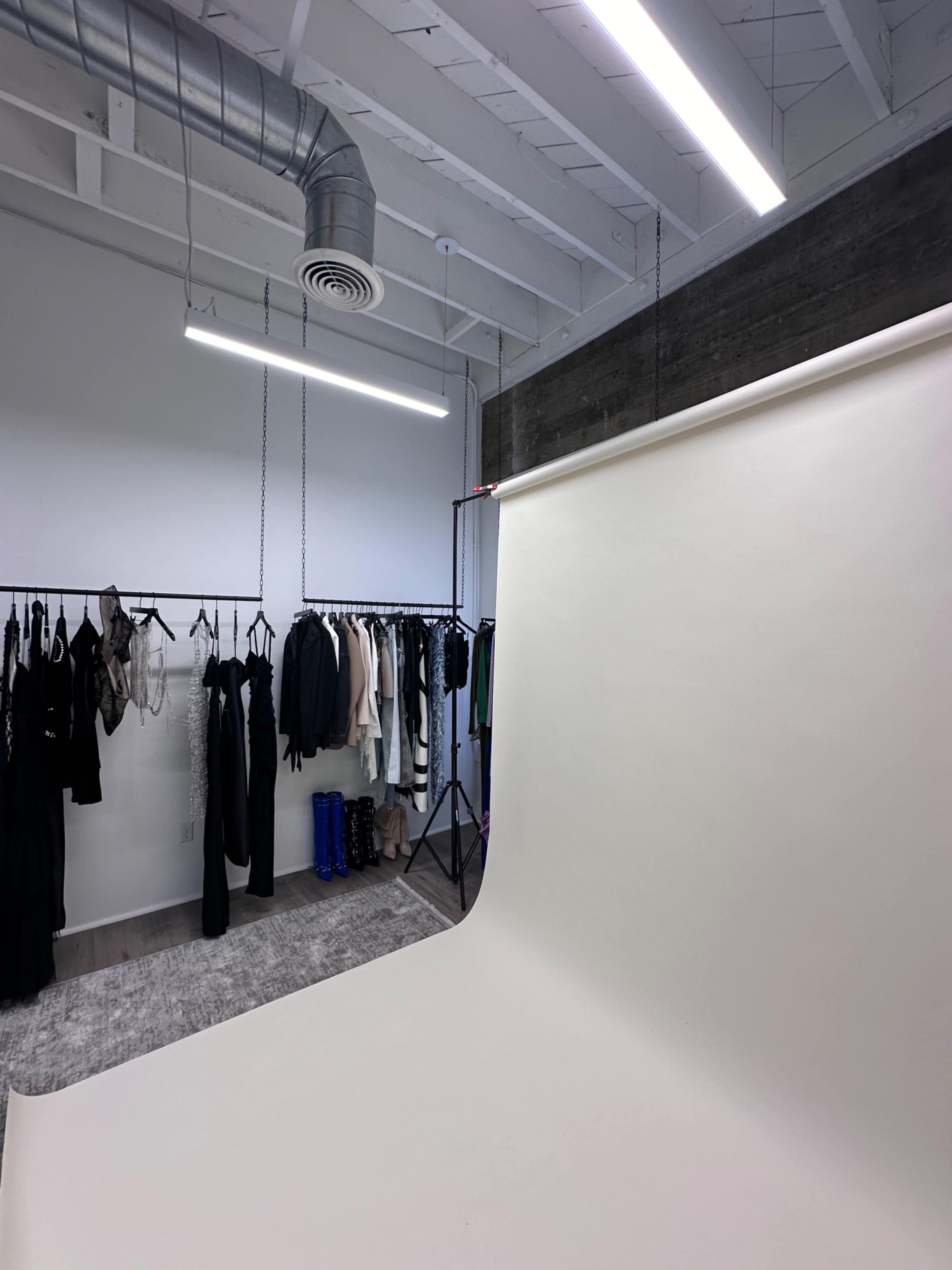 A photography studio with a seamless backdrop, hanging clothing on racks, and overhead lighting.