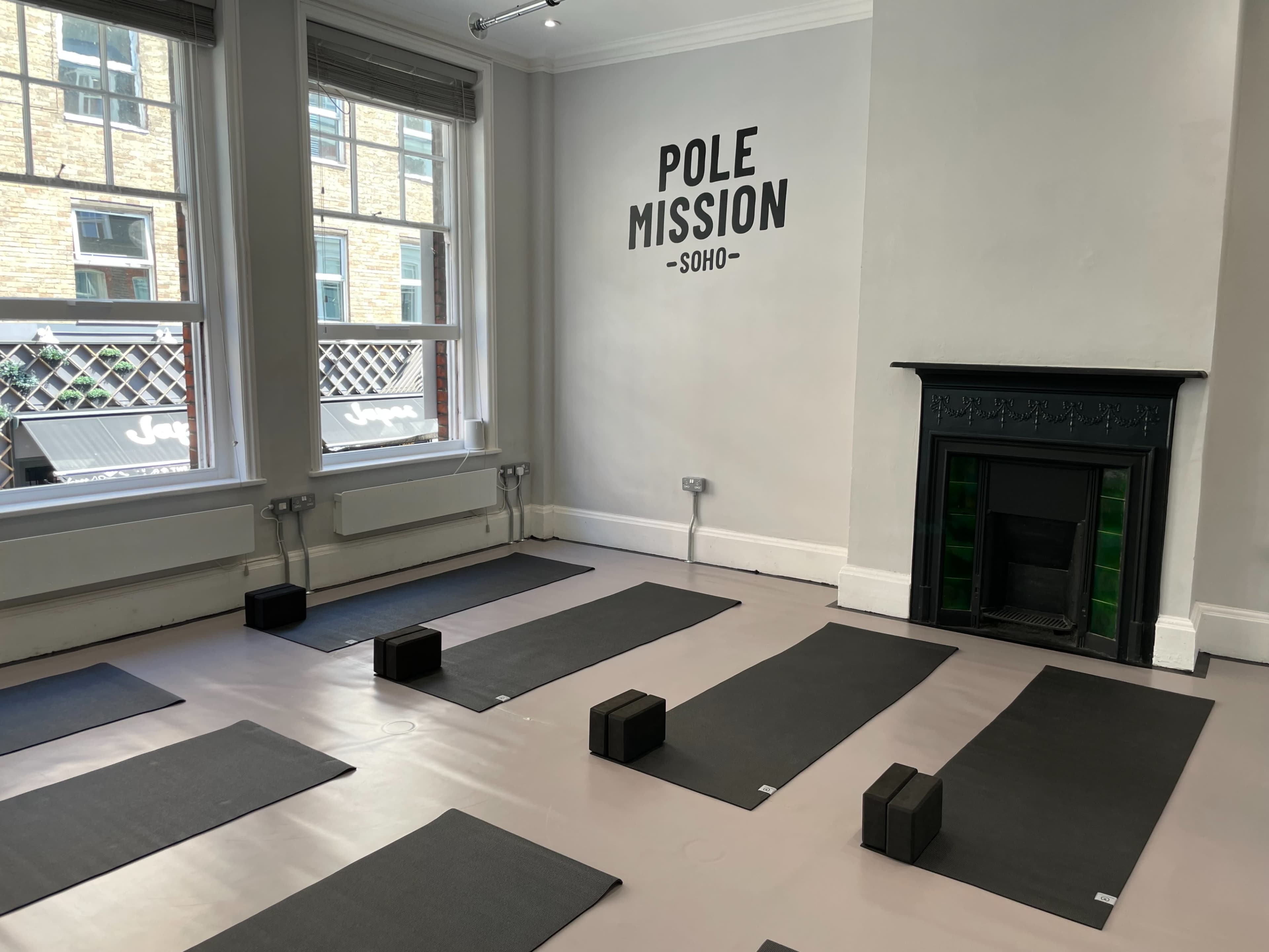 A yoga studio with mats arranged on a light-colored floor and a wall featuring the text "POLE MISSION - SOHO."