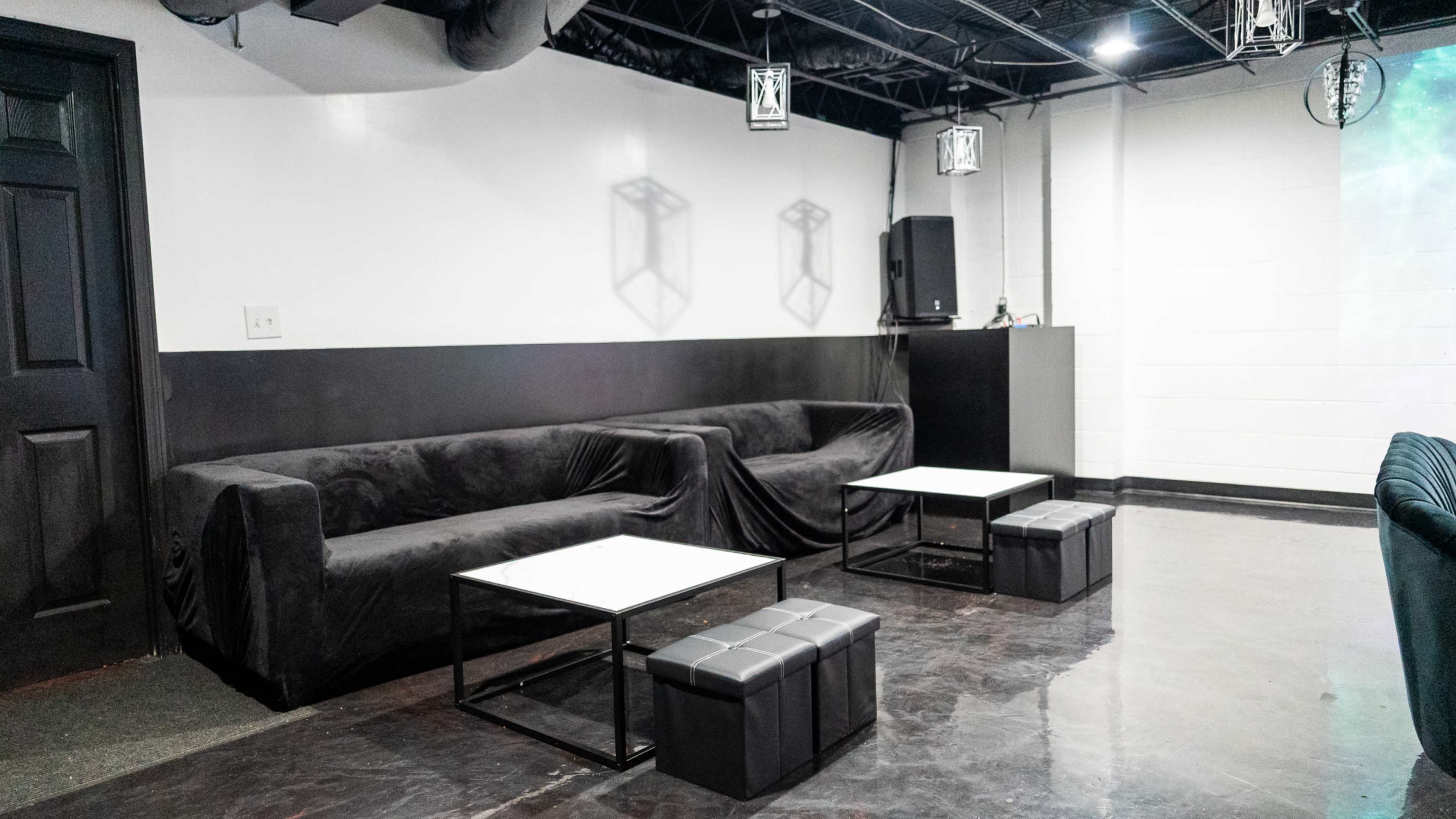 A modern lounge area featuring black sofas and minimalist coffee tables on a polished floor in a dimly lit room.