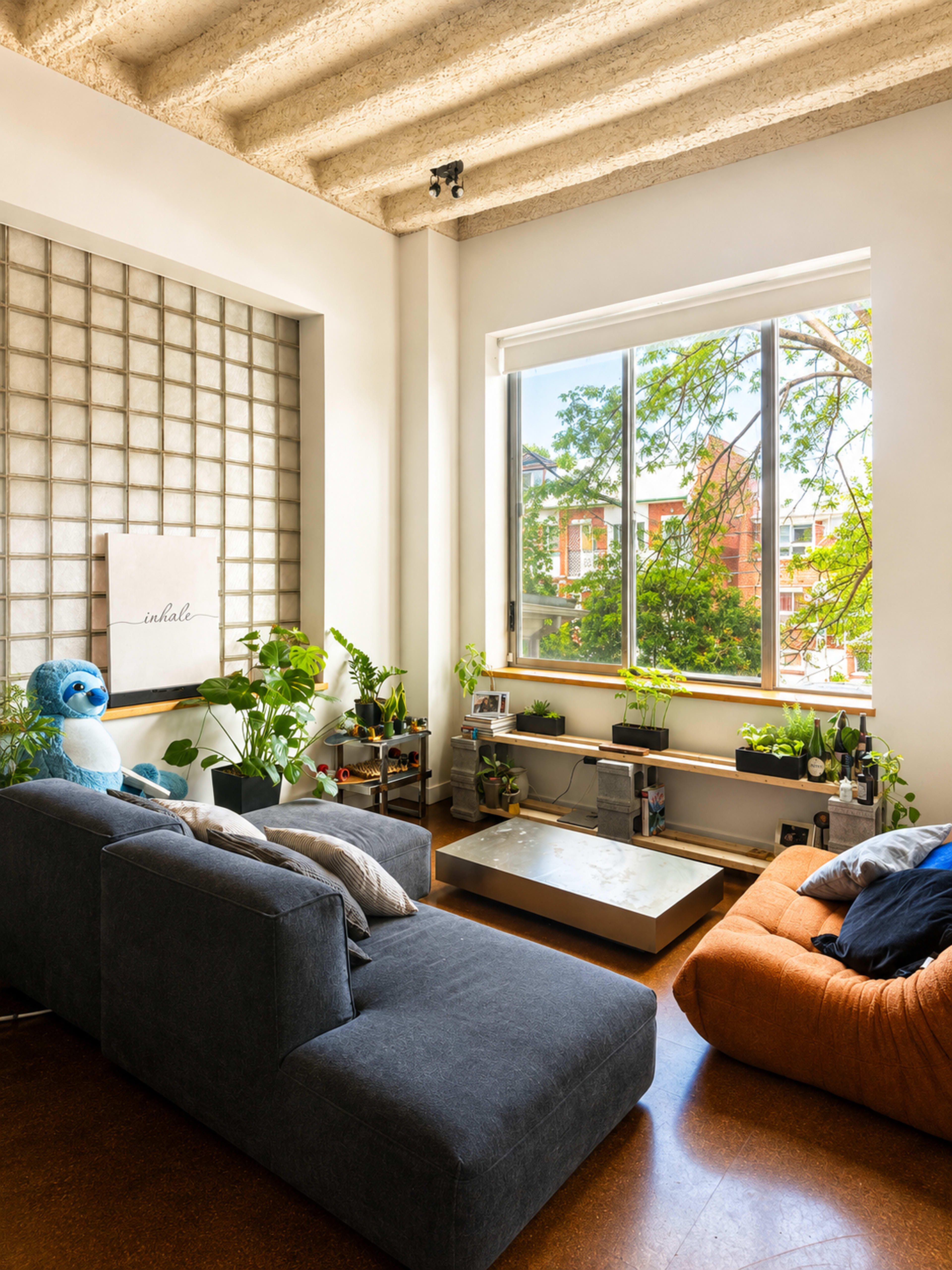 The image shows a bright living room with large windows, modern furniture, and several indoor plants.