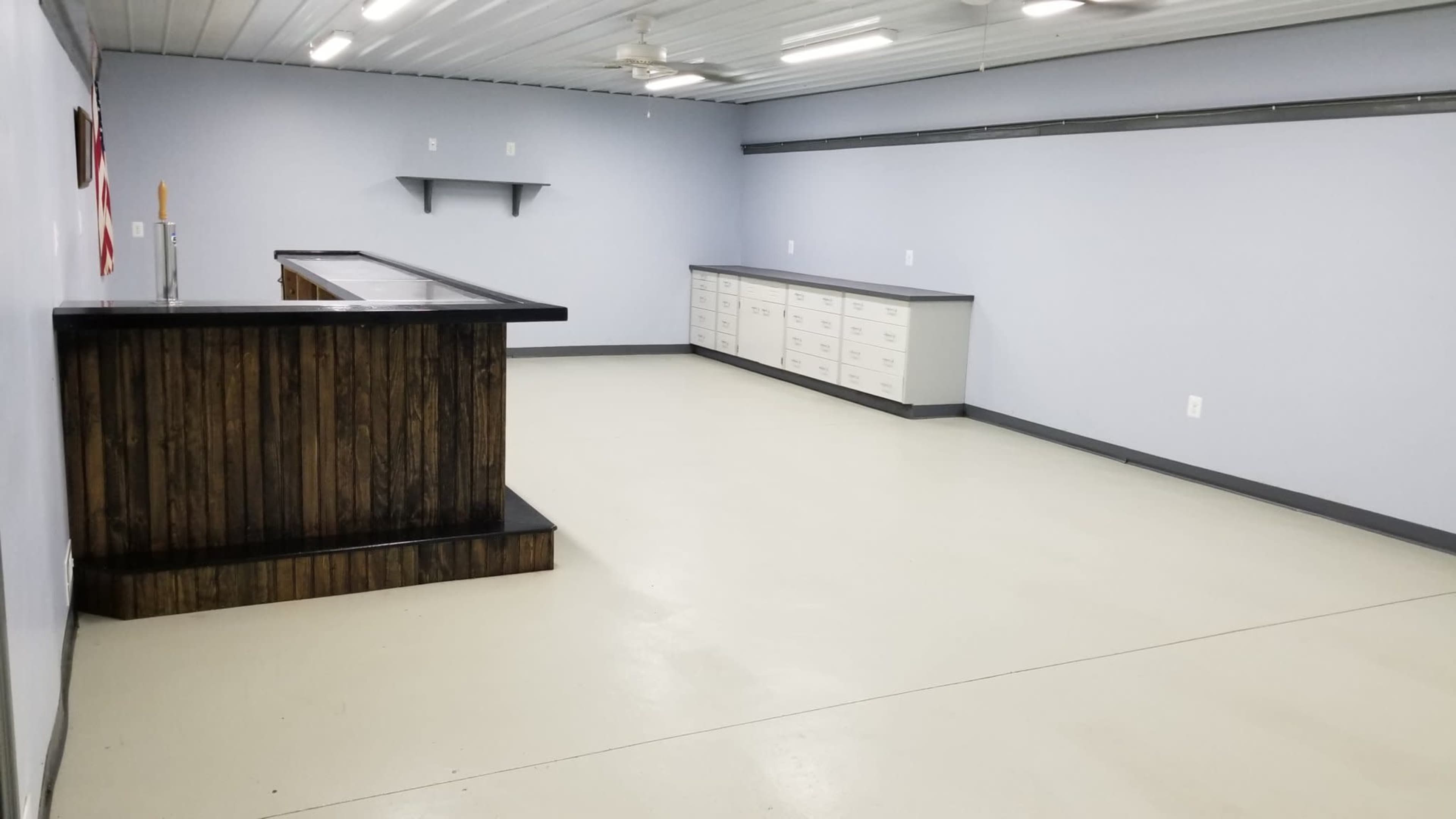 An empty room with light gray walls, a wooden bar counter, and cabinets along one side.