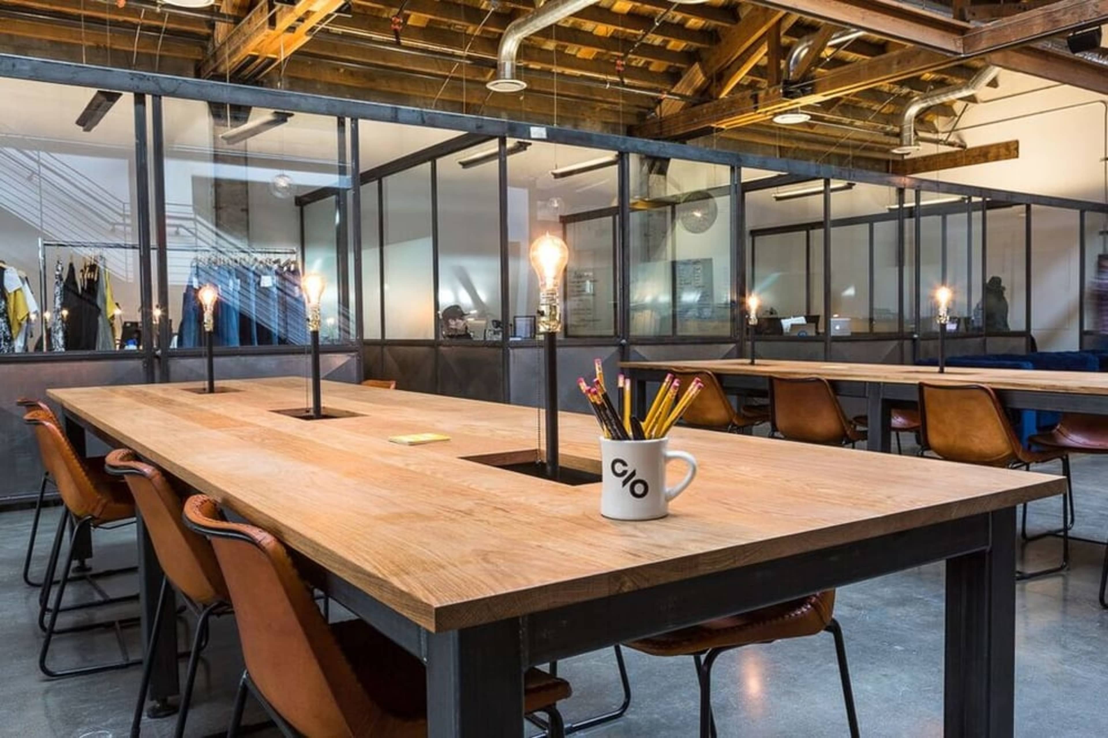 A spacious office features a large wooden table surrounded by leather chairs, with glass partitions and exposed beams overhead.